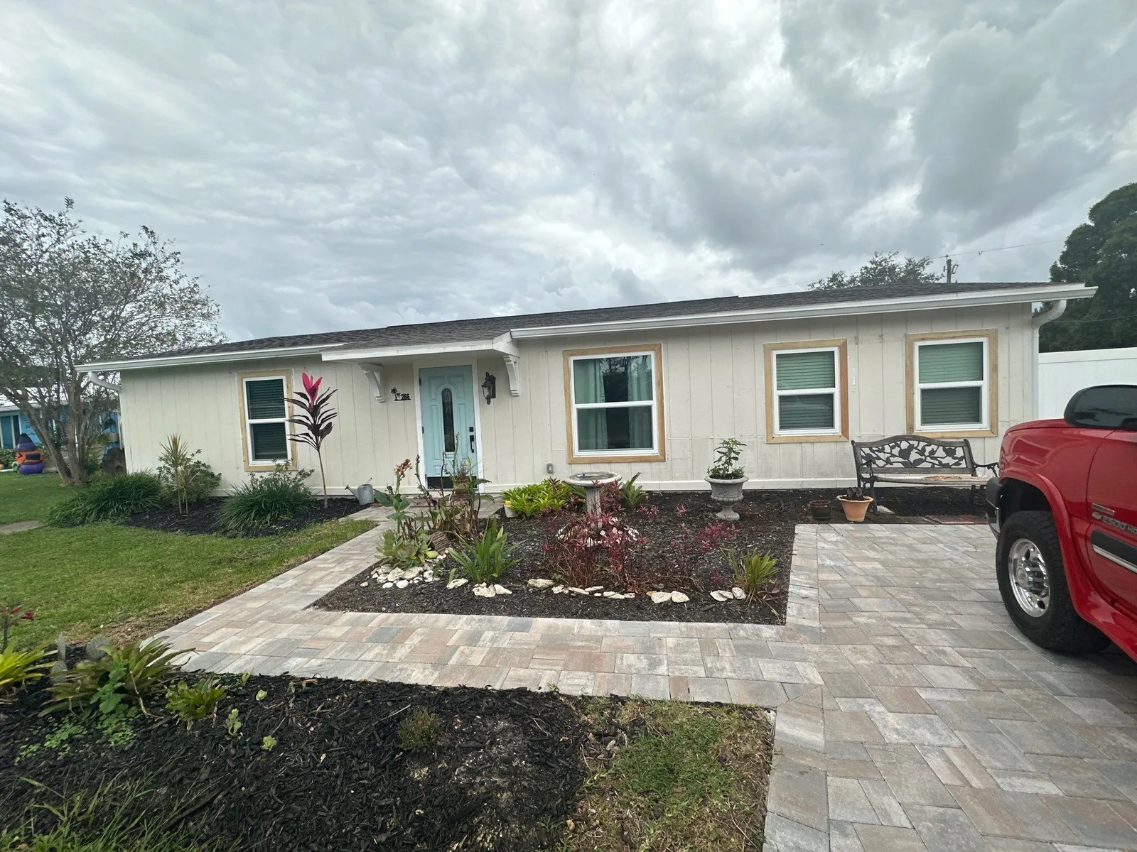 Exterior Painting in Port Saint Lucie, Florida. Single-storey home exterior with cream horizontal siding, white trim, a teal front door and a paver walkway with fresh landscaping.