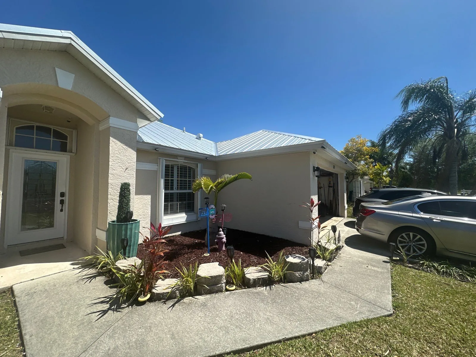 Exterior Painting in Port Saint Lucie, Florida. Angled view of a single-storey cream stucco home showing the front entry and side elevation with white trim and metal roof.