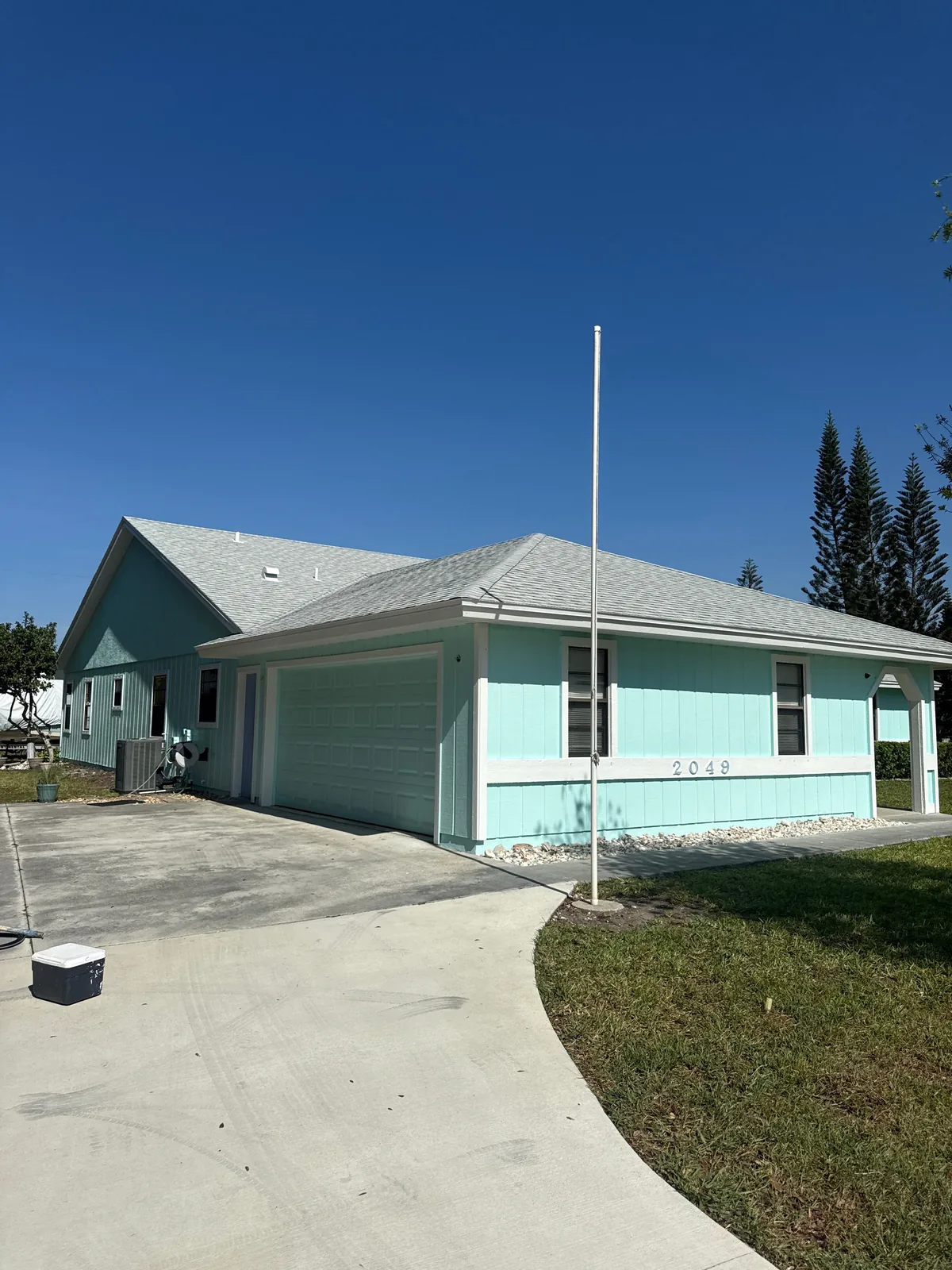 Exterior Painting in Port Saint Lucie, Florida. Single-storey house exterior painted light aqua with white trim and fascia, attached garage, concrete driveway and clear blue sky.
