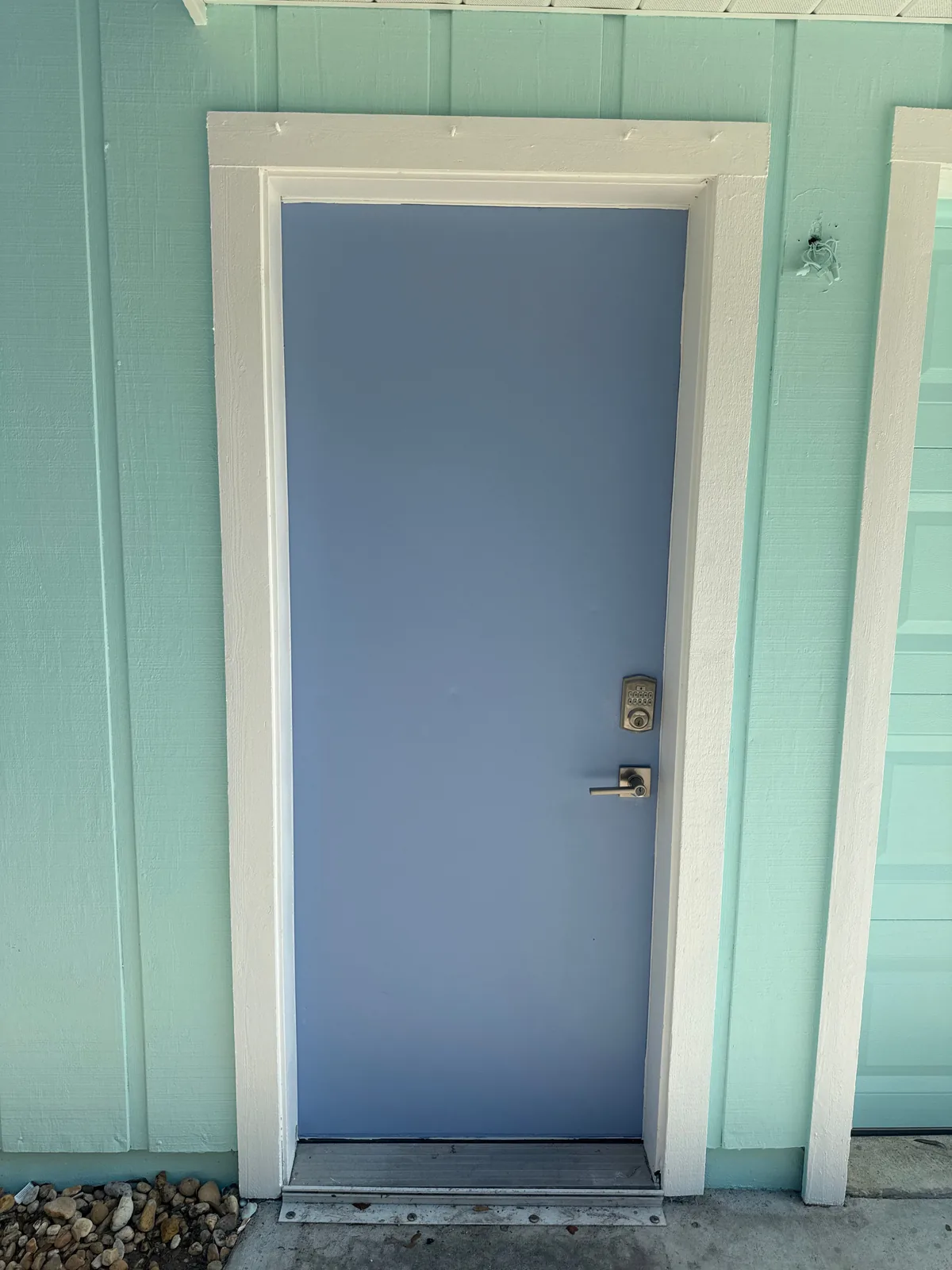 Exterior Painting in Port Saint Lucie, Florida. Exterior door painted periwinkle blue set in a white-trimmed frame against a mint green board-and-batten wall.