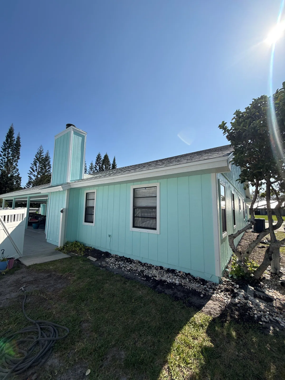 Exterior Painting in Port Saint Lucie, Florida. Single-storey house with mint green board-and-batten siding, white trim and a painted chimney, under a clear blue sky.