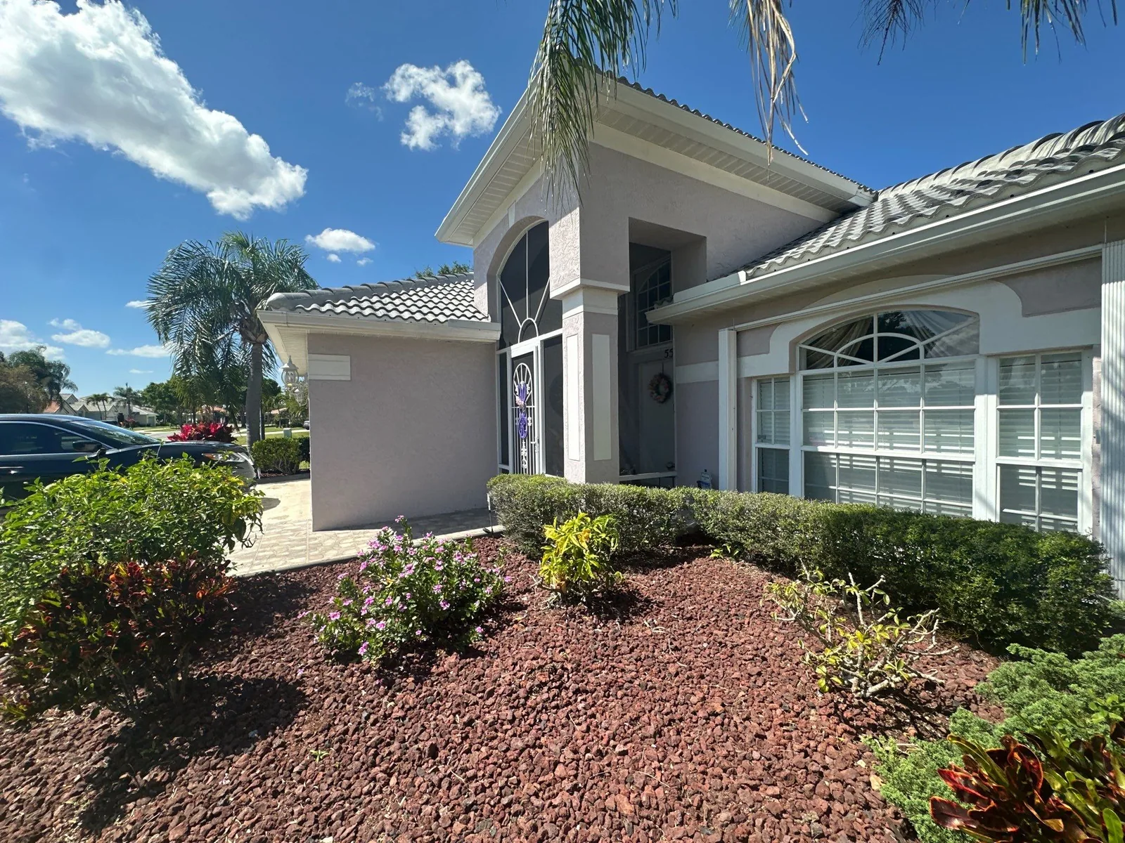 Exterior Painting in Port Saint Lucie, Florida. Front elevation of a single-storey stucco home with arched windows, tile roof and white trim.