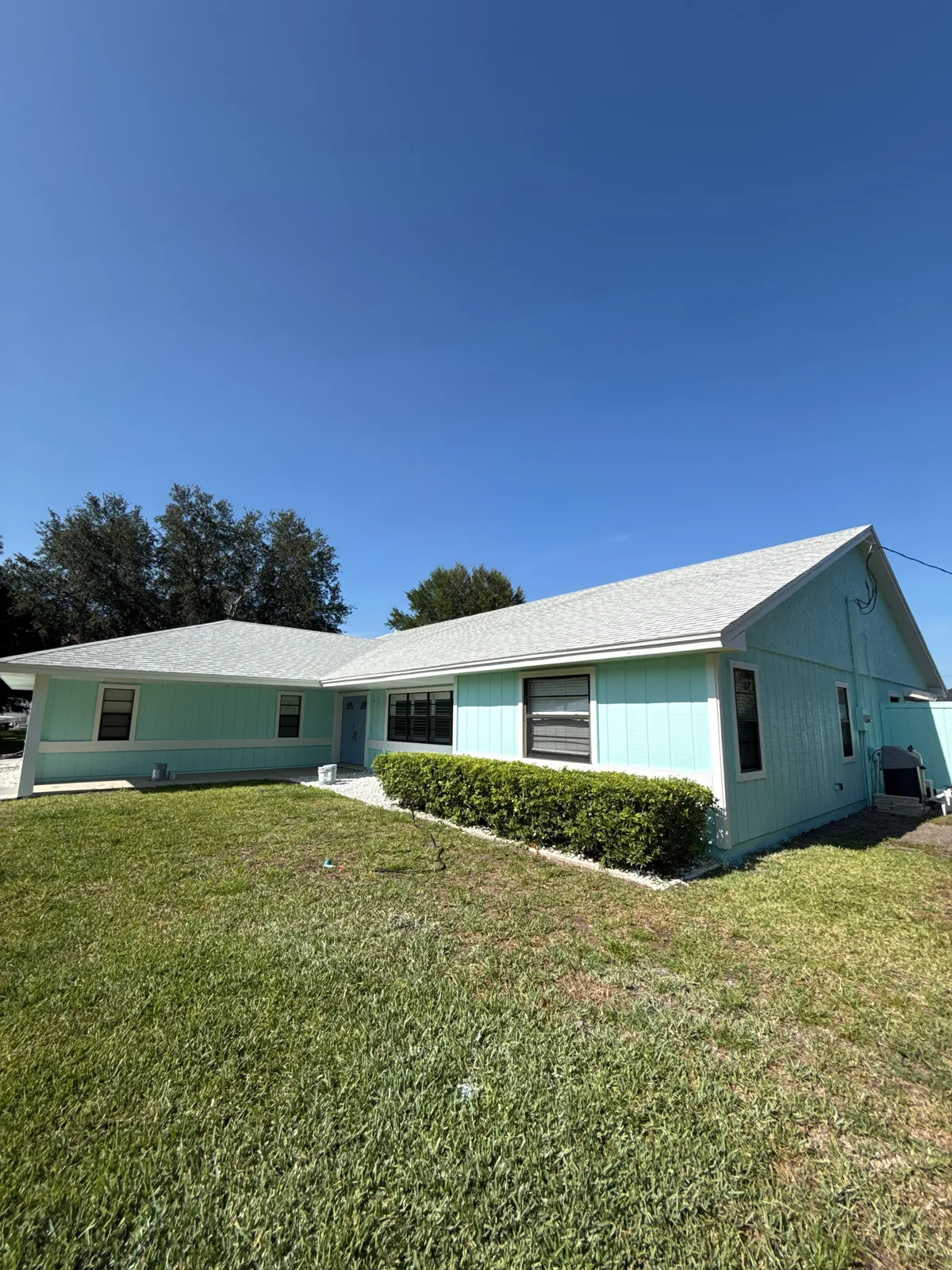 Exterior Painting in Port Saint Lucie, Florida. Single-storey house painted mint green with white trim, front hedges and a mown lawn under a blue sky.