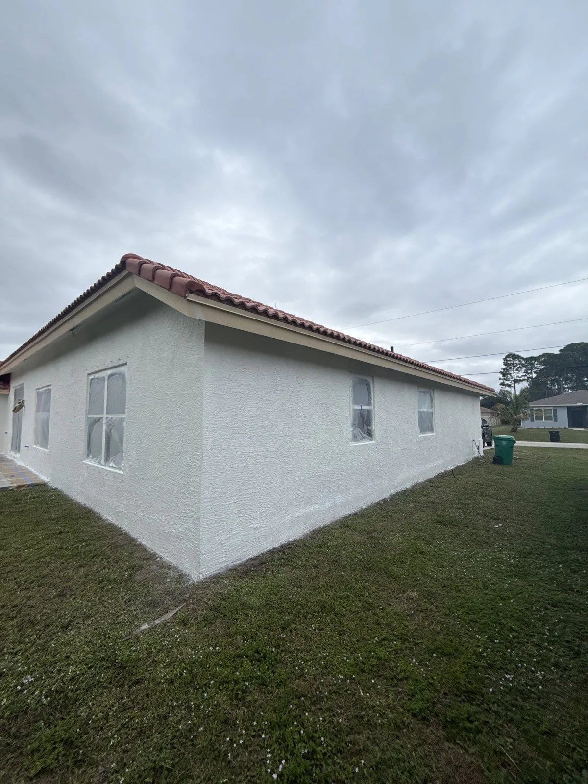 Exterior Painting in Port Saint Lucie, Florida. Corner view of a freshly painted white stucco single-storey house with barrel tile roof and green lawn.