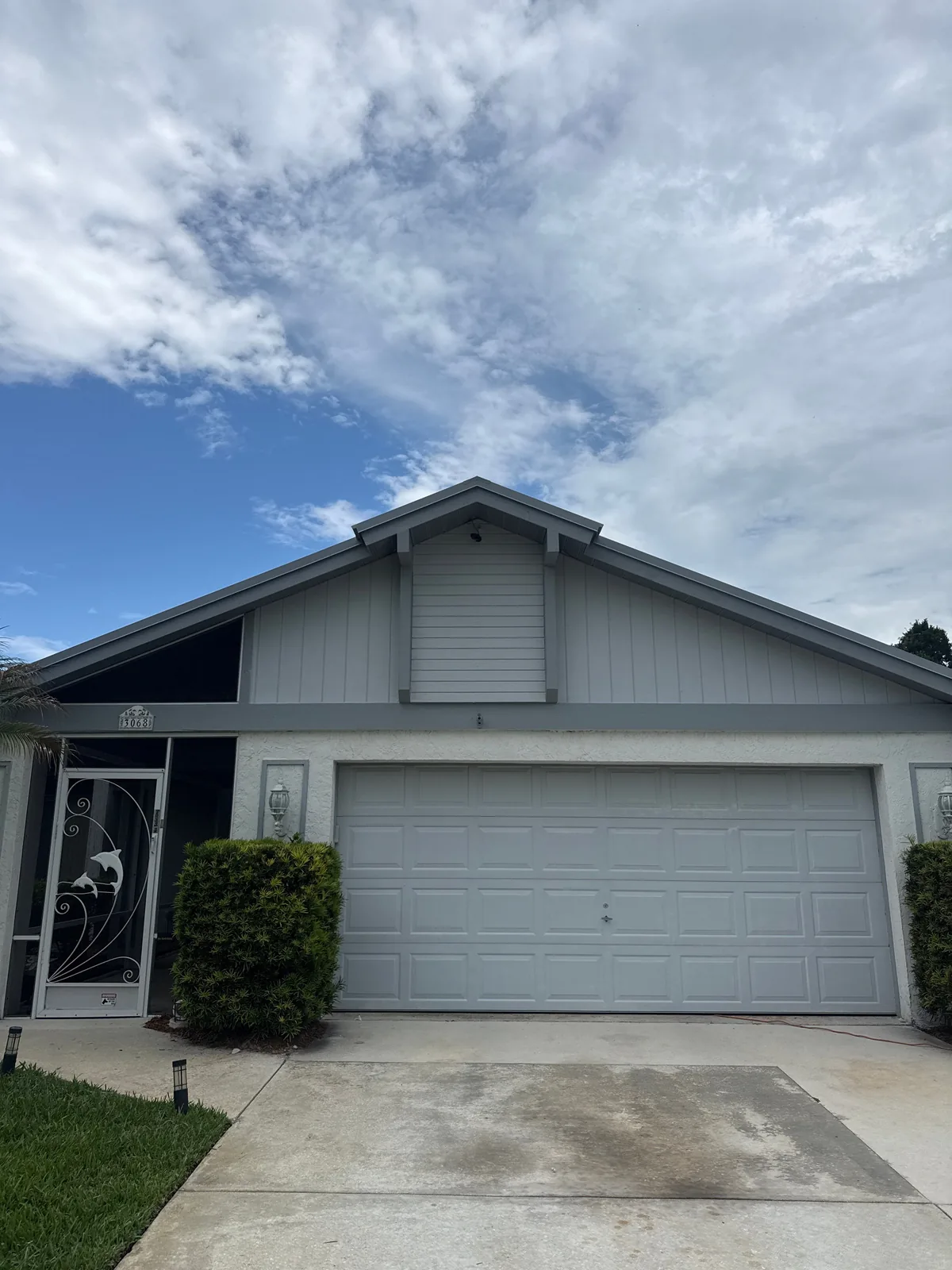 Exterior Painting in Port Saint Lucie, Florida. Single-storey house exterior, grey board-and-batten gable end with white trim, light grey garage door.