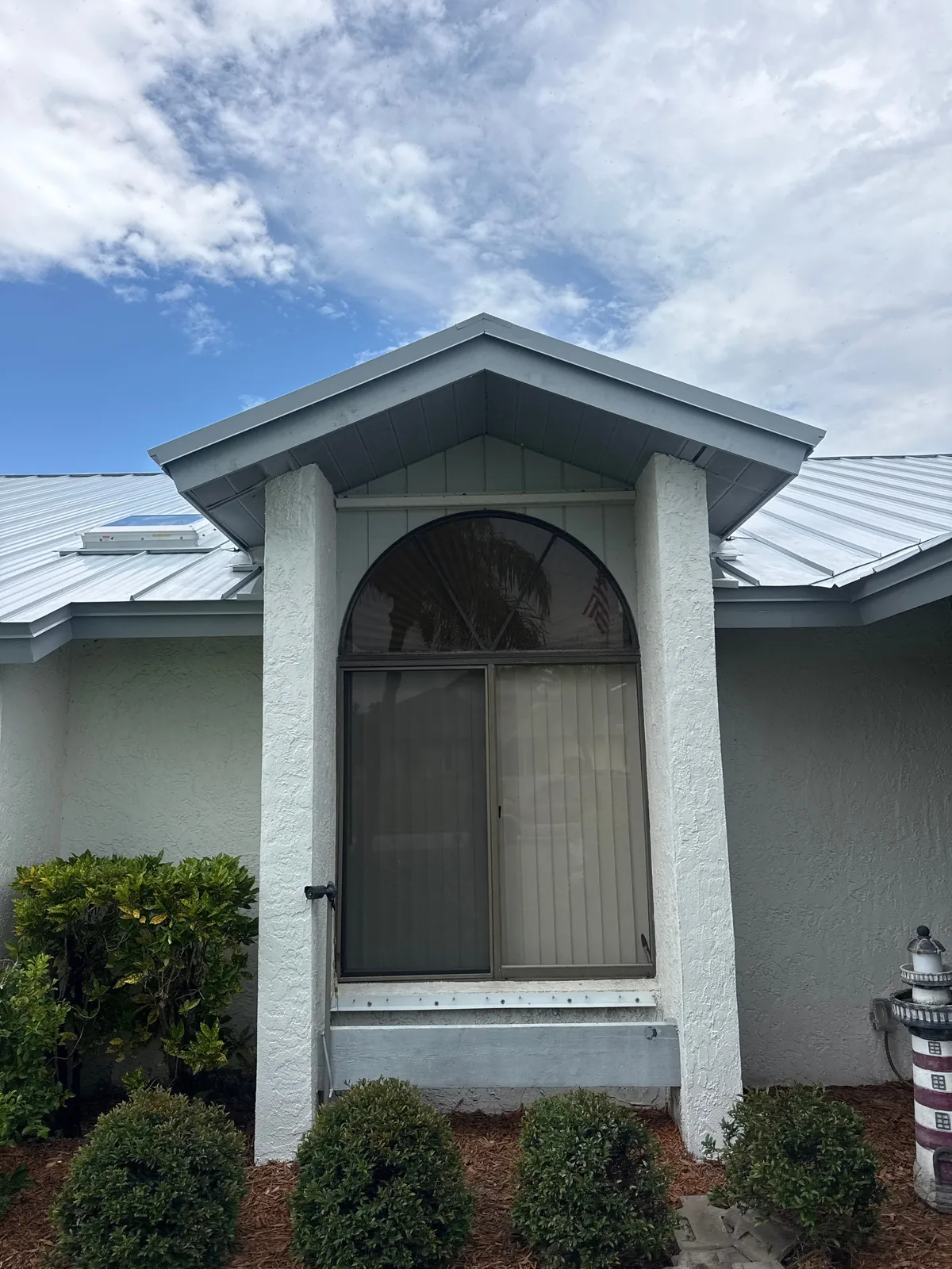 Exterior Painting in Port Saint Lucie, Florida. White stucco house entry with gabled portico, arched screened door and white trim under a metal roof.