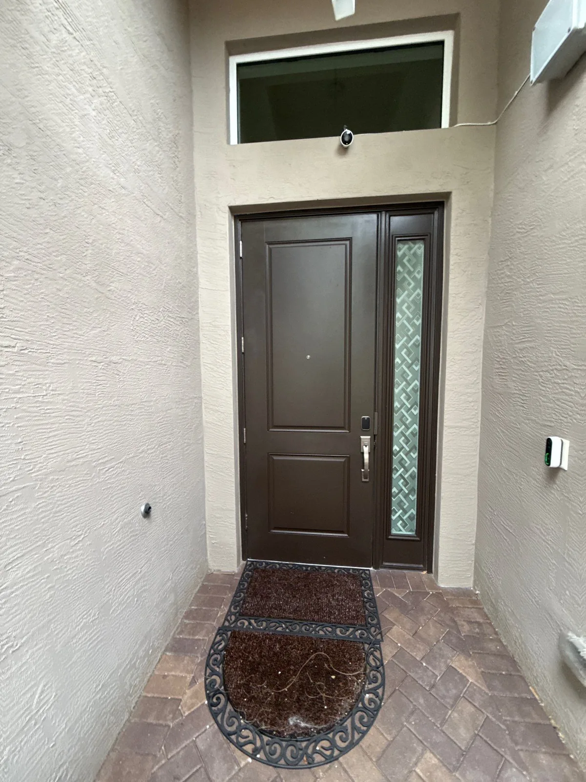 Exterior Painting in Port Saint Lucie, Florida. Recessed front entry with a dark brown painted front door and decorative glass sidelight, tan stucco walls and a paver landing.