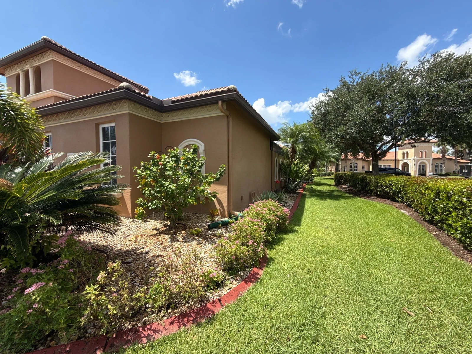Exterior Painting in Port Saint Lucie, Florida. Side elevation of a two-storey stucco home in tan with a terracotta barrel tile roof, arched window and landscaped bed along the lawn.