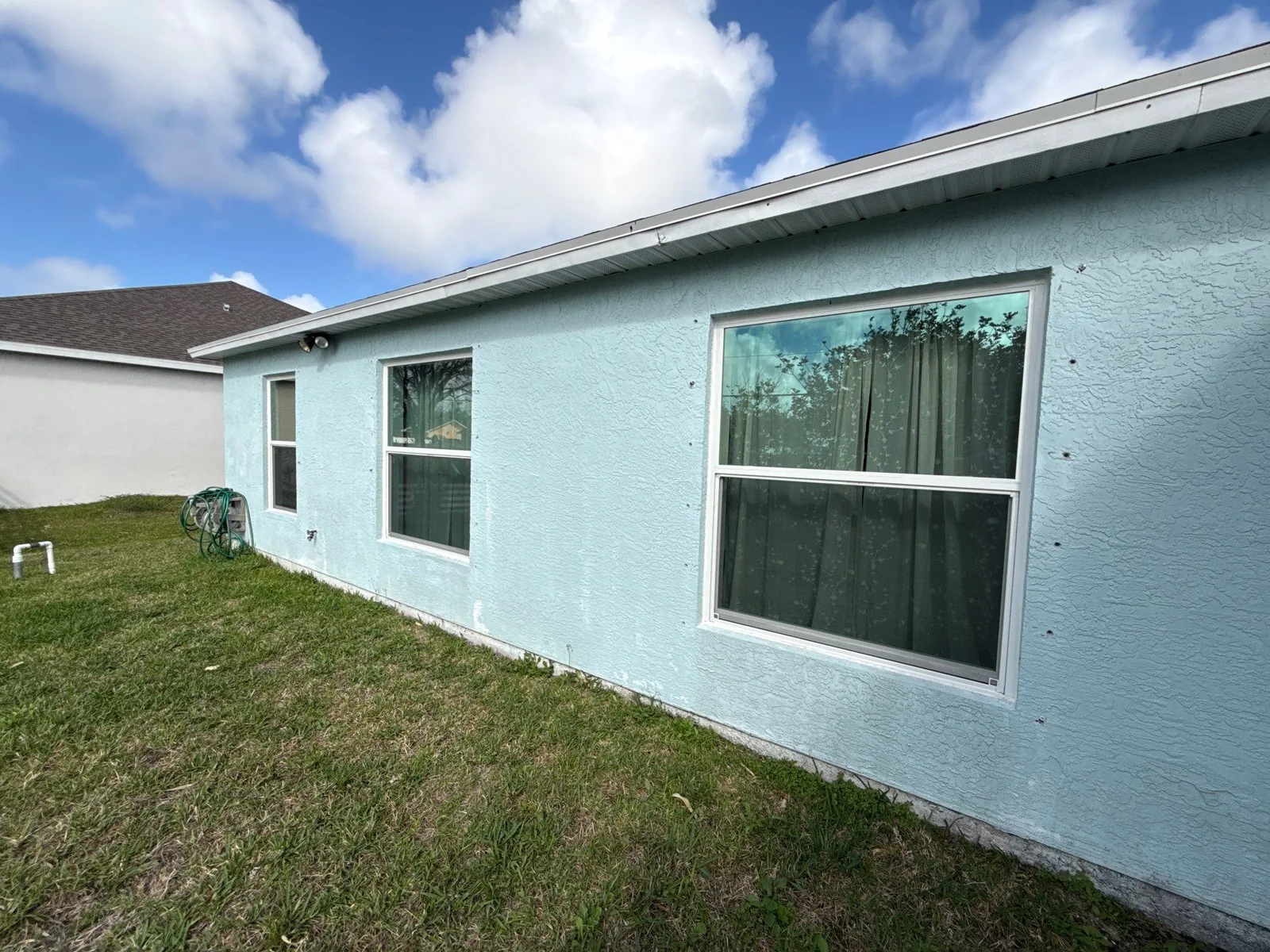 Exterior Painting in Port Saint Lucie, Florida. Side elevation of a single-storey pale blue stucco house with white-trimmed windows under a blue sky.