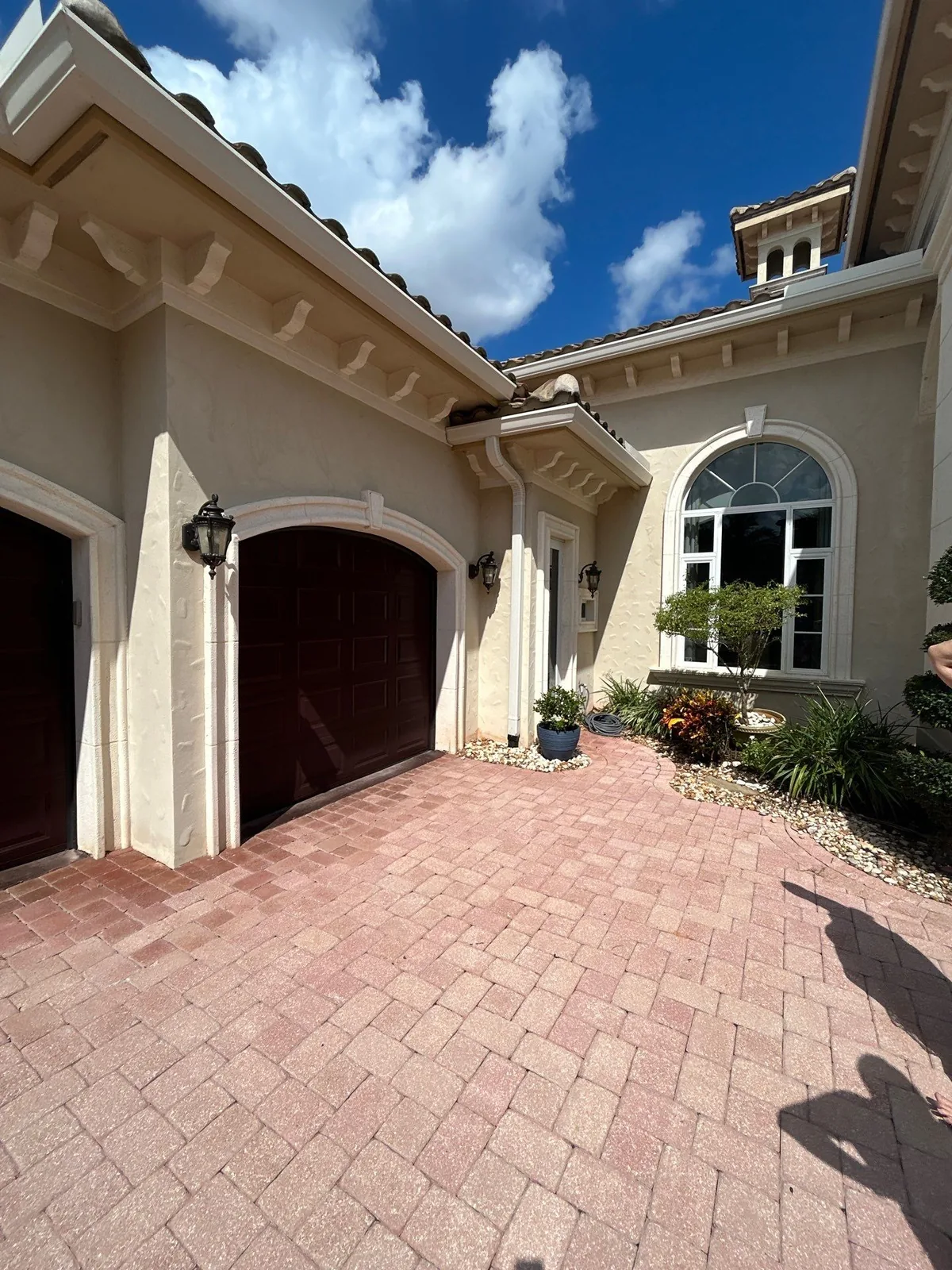 Exterior Painting in Port Saint Lucie, Florida. Stucco home front elevation with two arched garage doors, coach lights, tile roof and a paver driveway.