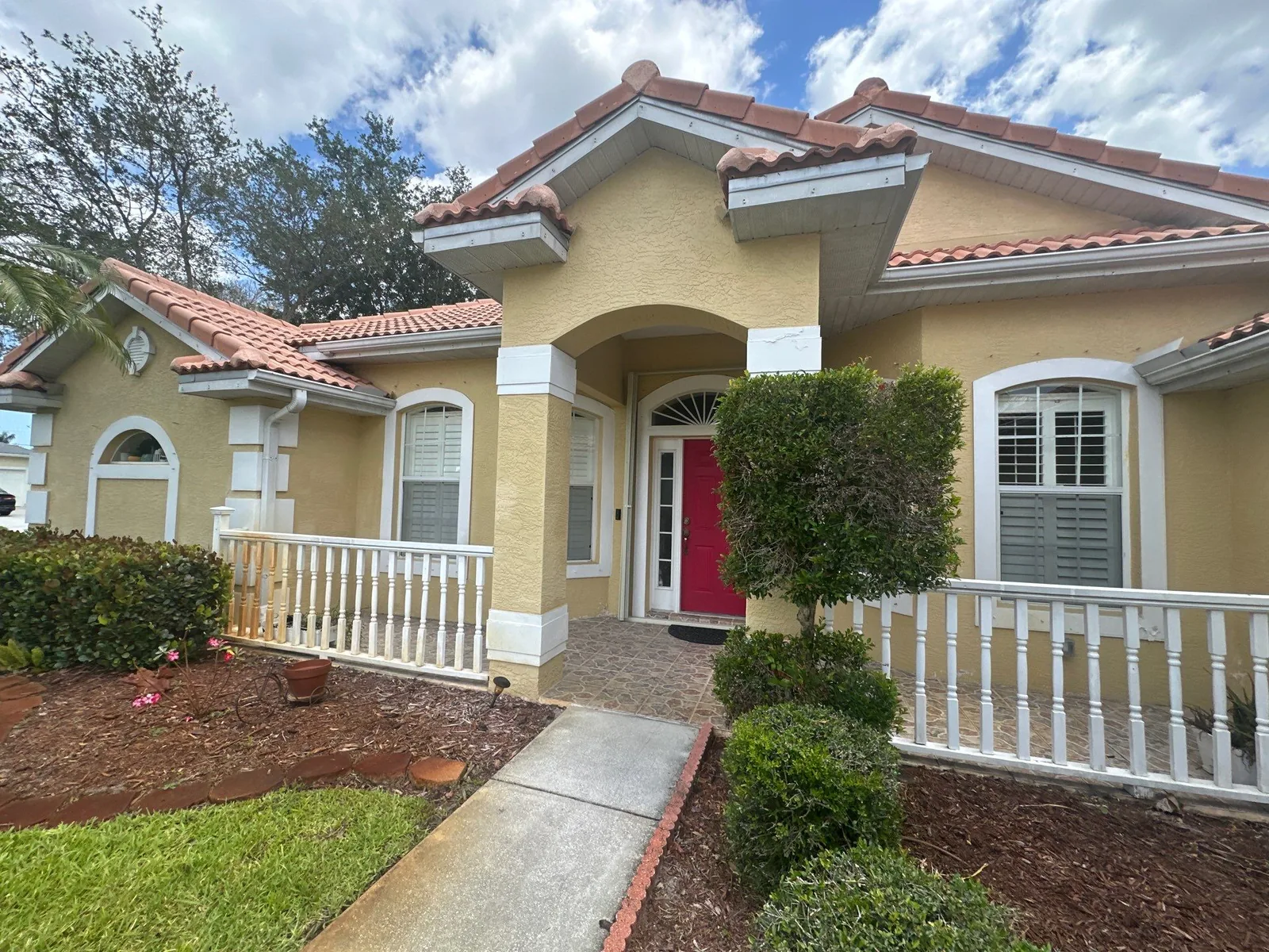 Exterior Painting in Port Saint Lucie, Florida. Yellow stucco home entry with white trim, red front door, white porch railing and barrel tile roof.