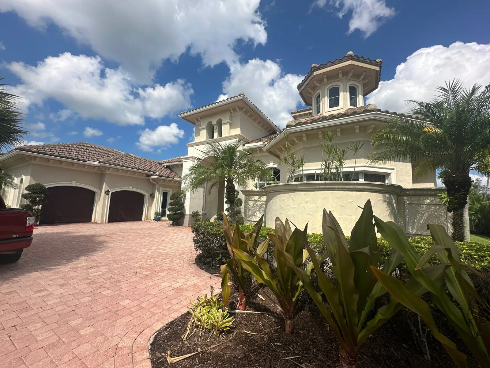 Exterior Painting in Port Saint Lucie, Florida. Two-storey stucco home with barrel tile roof, turret with balcony, arched garage bays and brick paver driveway.