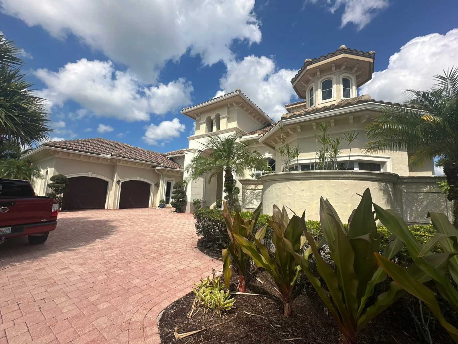 Exterior Painting in Port Saint Lucie, Florida. Front elevation of a two-storey cream stucco home with tile roof, turret, arched garage doors and paver driveway.