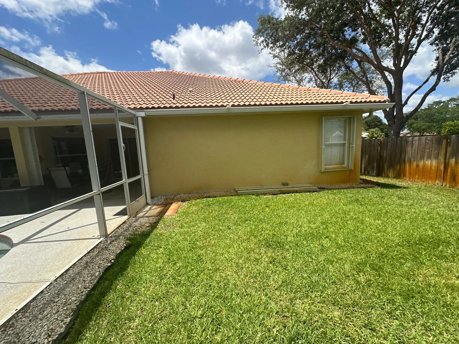 Exterior Painting in Port Saint Lucie, Florida. Rear elevation of a single-storey tan stucco home with barrel tile roof, shuttered window and screened pool enclosure.