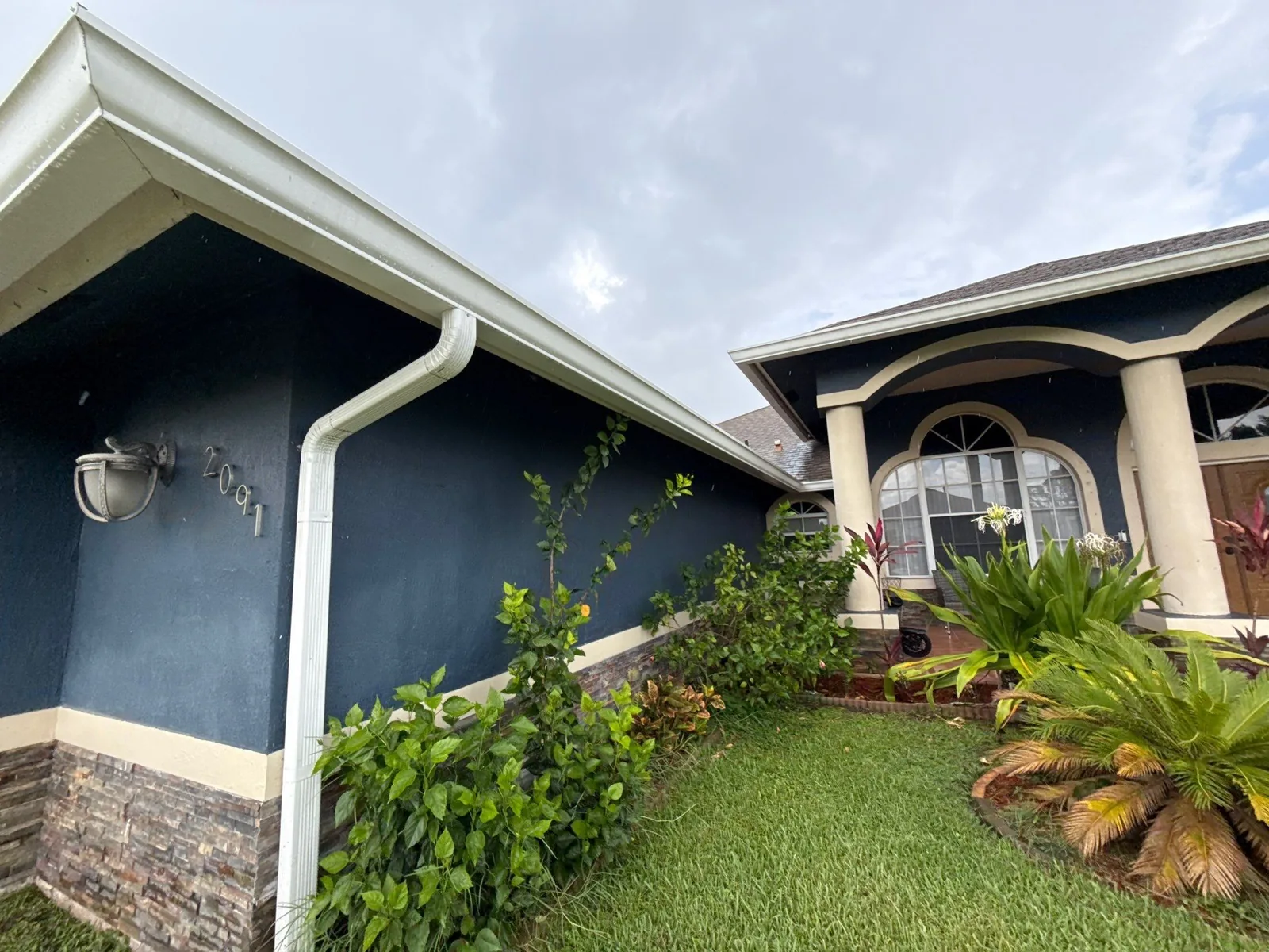 Exterior Painting in Port Saint Lucie, Florida. Navy blue stucco exterior with white fascia and gutters, stone base accent and arched entry columns.