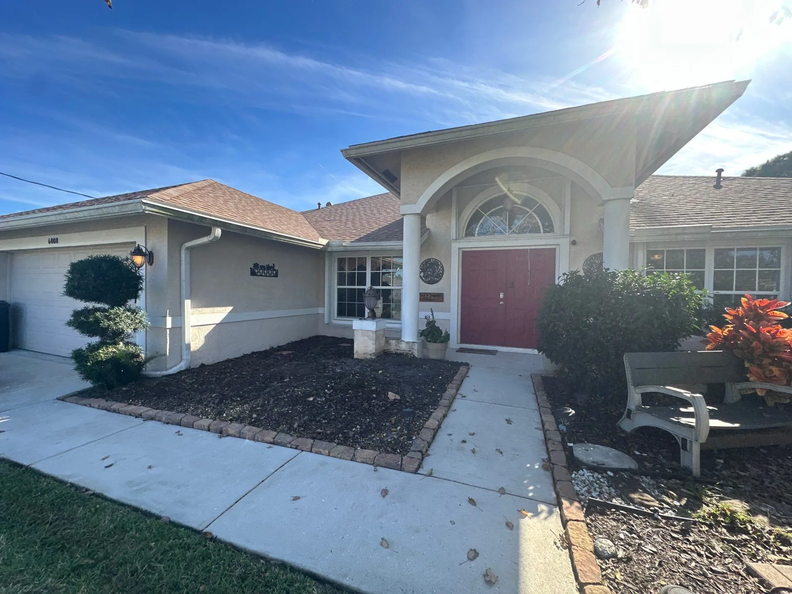 Exterior Painting in Port Saint Lucie, Florida. Single-storey stucco home with an arched entry, red front door and white trim, under blue sky.