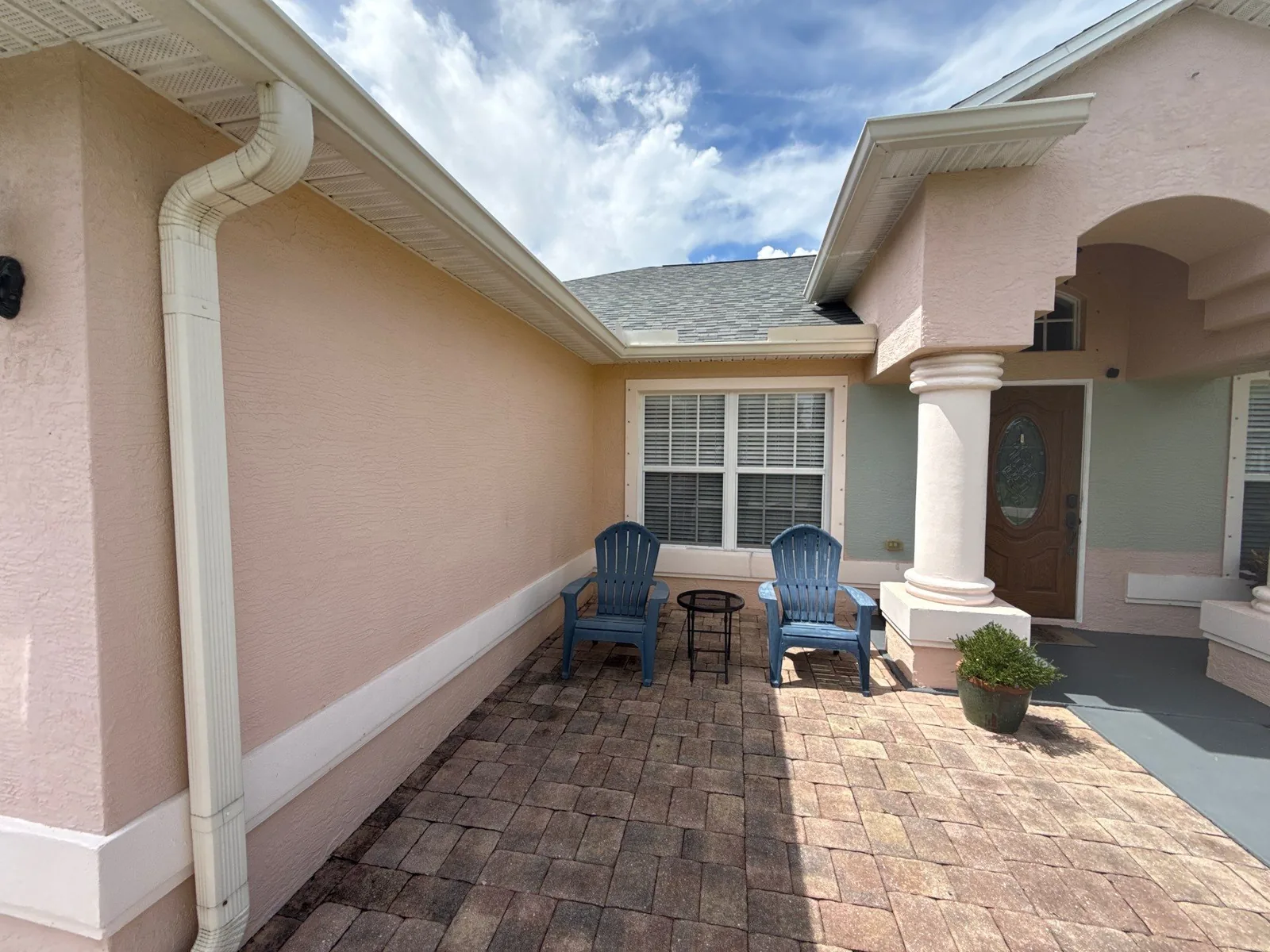 Exterior Painting in Port Saint Lucie, Florida. Courtyard entry of a home with pale pink stucco walls, white gutters and trim, patio chairs on a paver courtyard.