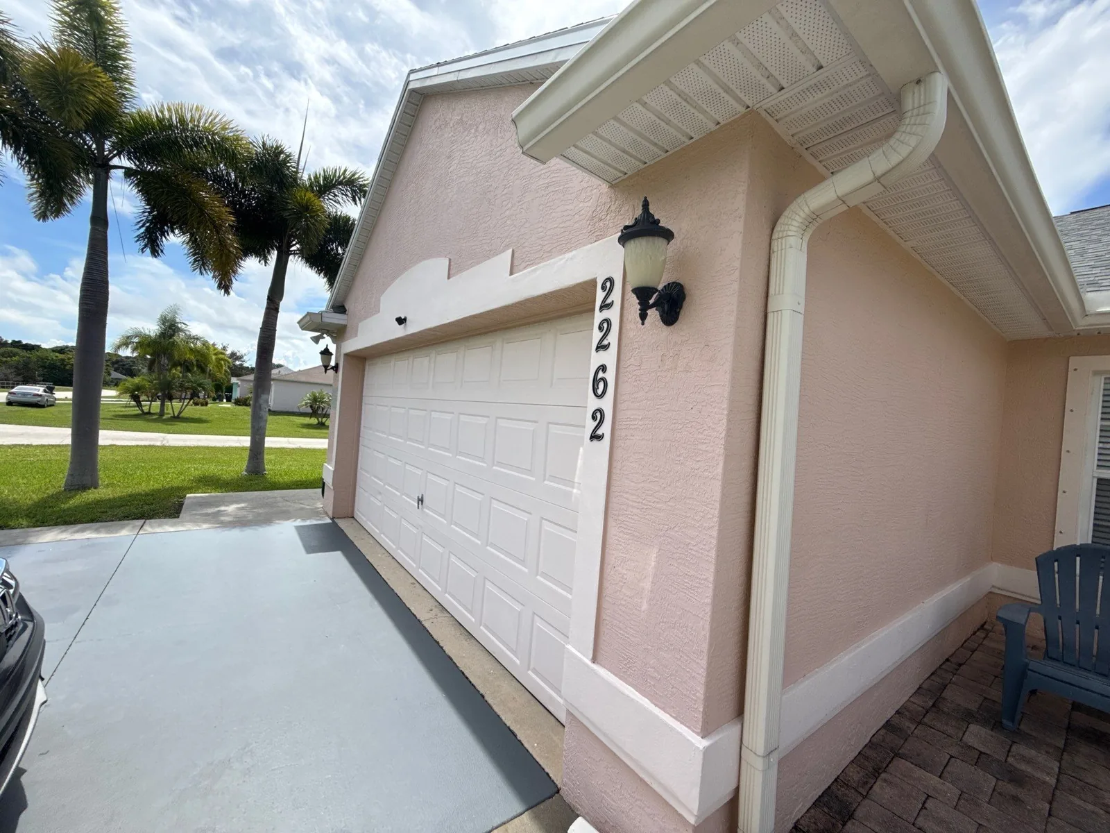 Exterior Painting in Port Saint Lucie, Florida. Garage elevation of a home with pale pink stucco, white sectional garage door and white base trim, palms and concrete drive.