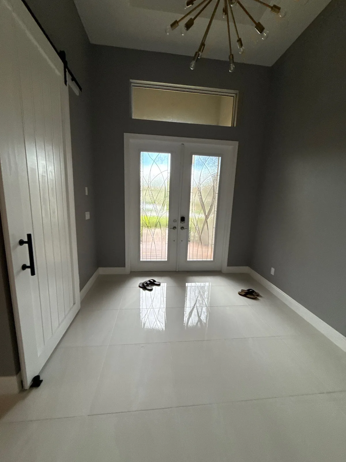 Interior Painting in Port Saint Lucie, Florida. Entry room with grey walls, white sliding barn door, white trim and glazed double doors over large-format tile.
