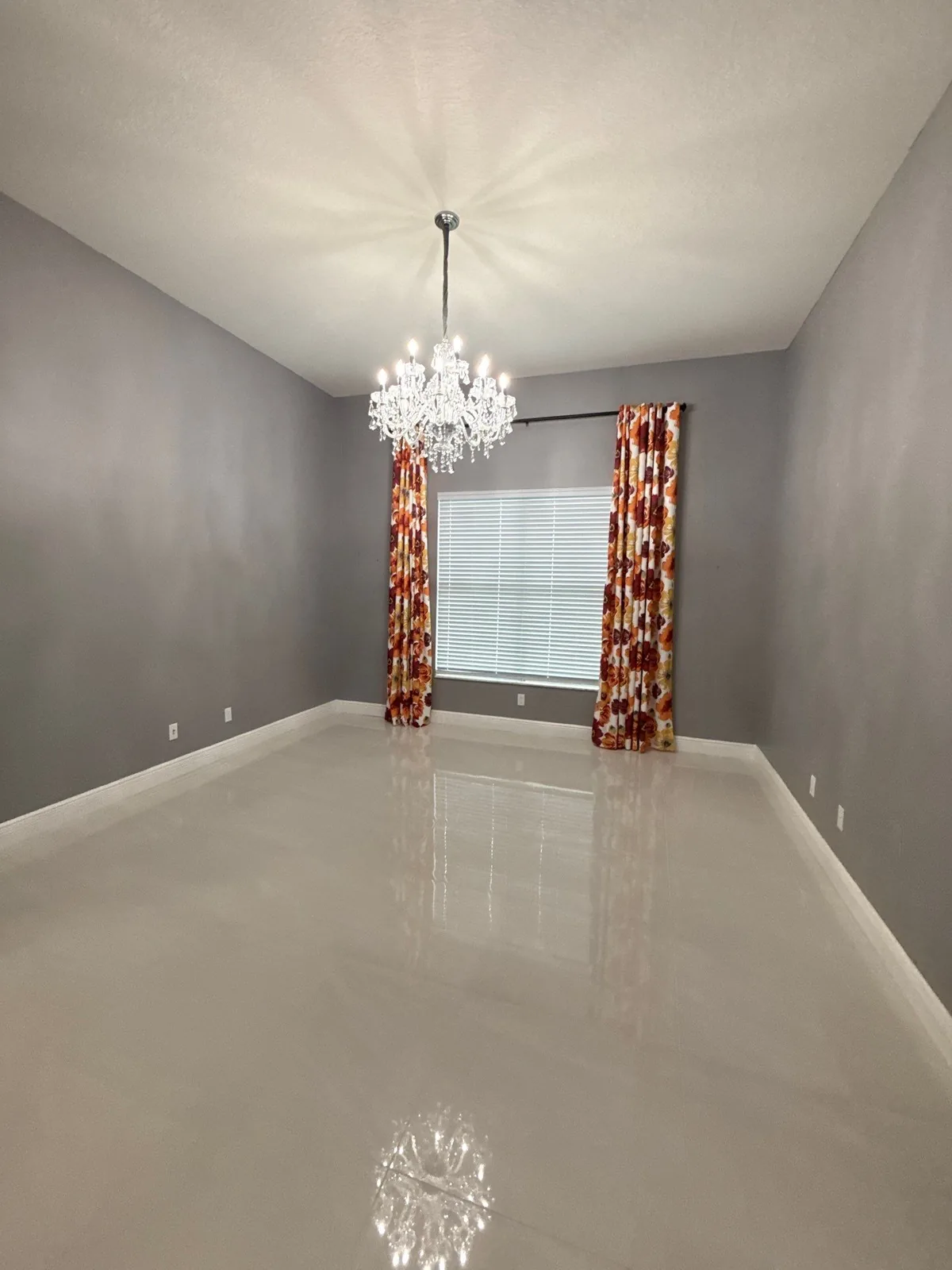 Interior Painting in Port Saint Lucie, Florida. Empty dining room with grey painted walls, white ceiling, chandelier and patterned curtains at a shuttered window.