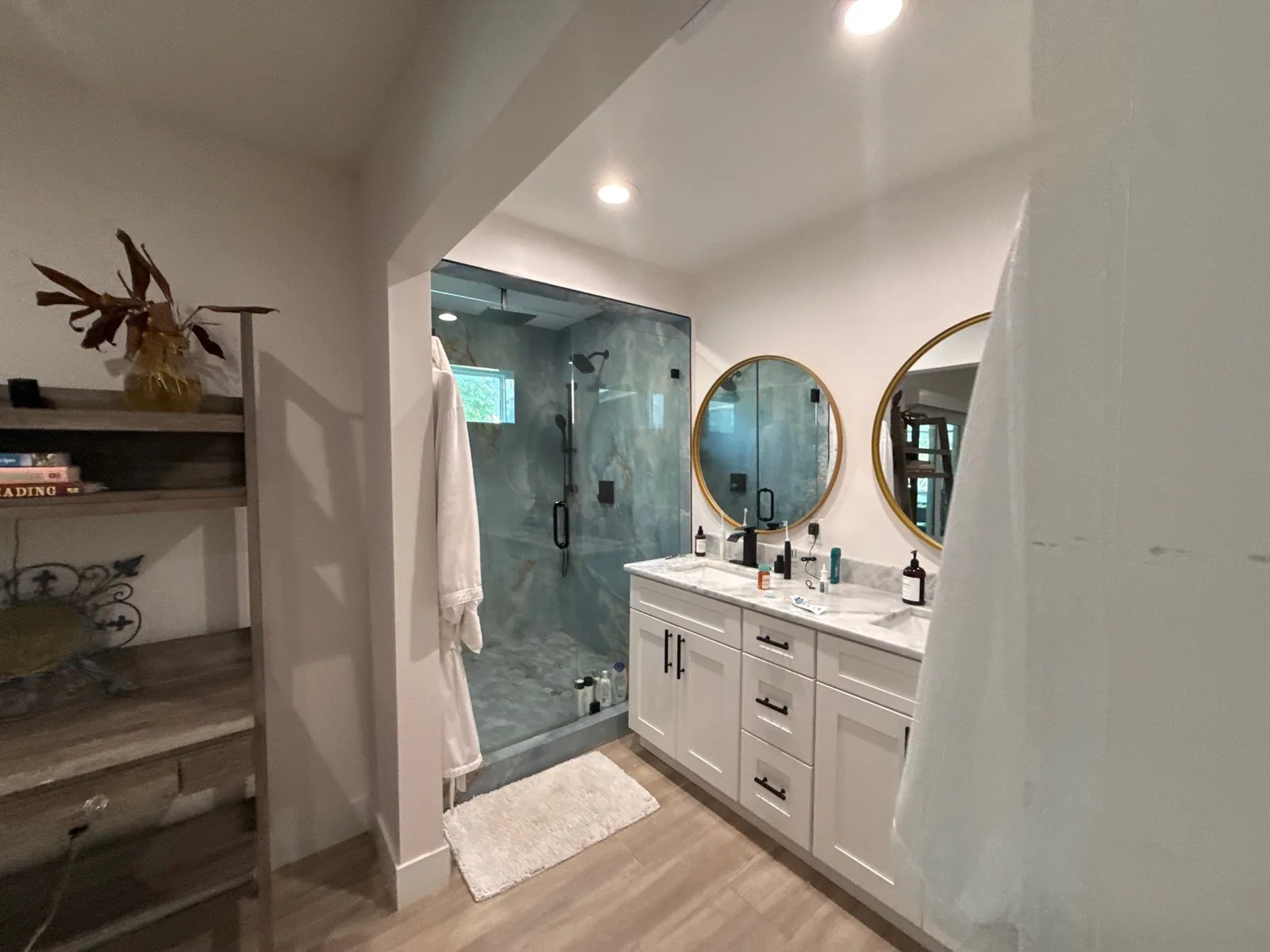 Interior Painting in Port Saint Lucie, Florida. Bathroom with white walls, a white double vanity with two round gold-framed mirrors and a tiled walk-in shower with glass door.