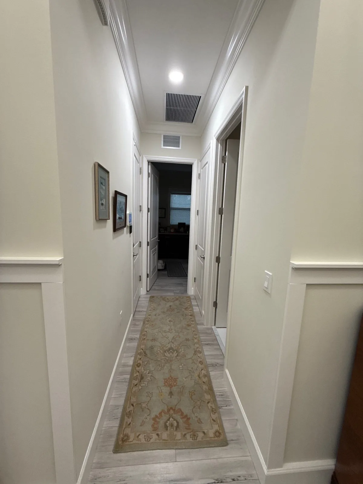 Interior Painting in Port Saint Lucie, Florida. Interior hallway with white painted walls, wainscoting, crown moulding and a runner rug leading to doorways.
