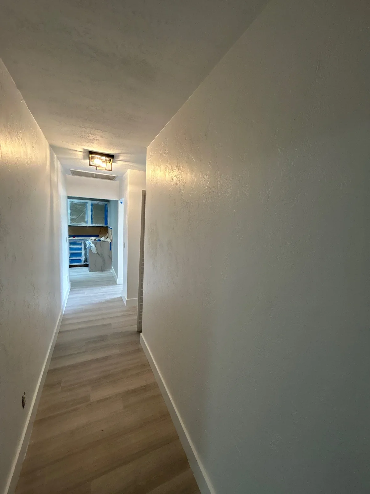 Interior Painting in Port Saint Lucie, Florida. Hallway with freshly painted white walls and ceiling, flush ceiling light and wood-look flooring.