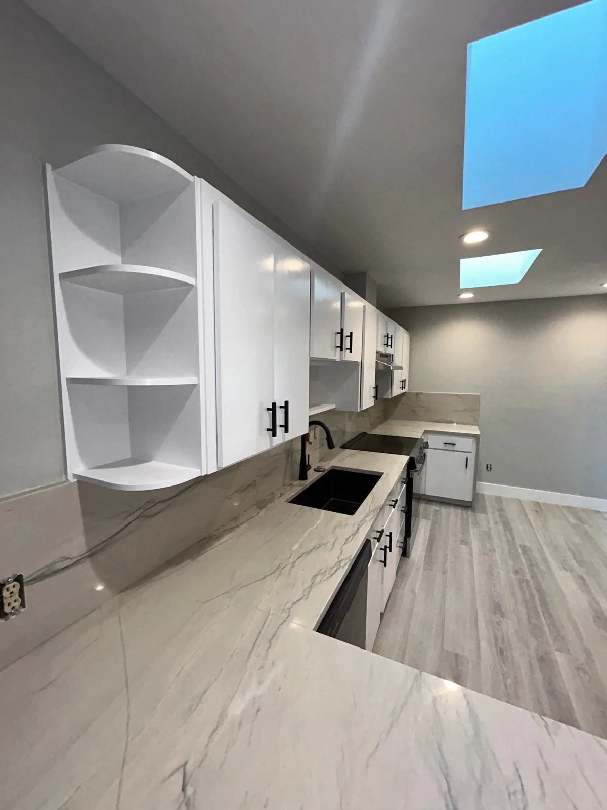 Interior Painting in Port Saint Lucie, Florida. Galley kitchen with white upper and lower cabinets, marble-pattern countertops and backsplash, grey painted walls and a skylight.