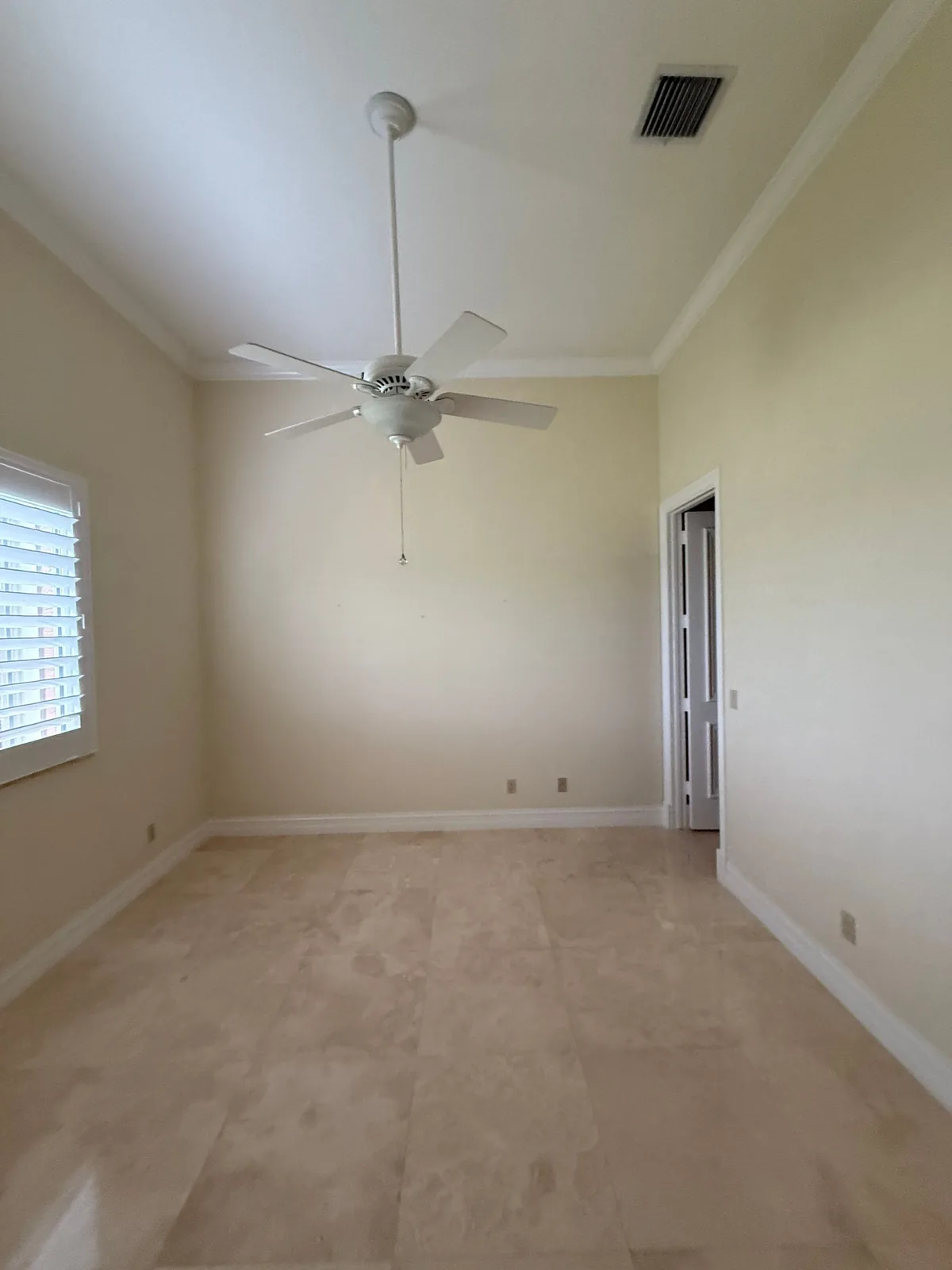 Interior Painting in Port Saint Lucie, Florida. Empty bedroom with pale walls, white crown moulding and baseboards, white ceiling fan and tile flooring.