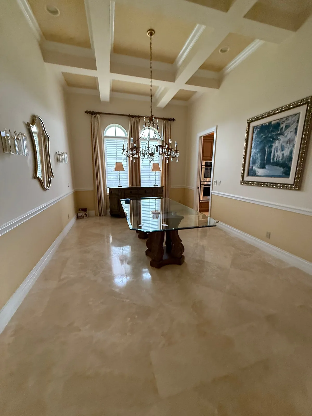 Interior Painting in Port Saint Lucie, Florida. Formal dining room with painted coffered ceiling, cream and white two-tone walls, chandelier and glass-top table.