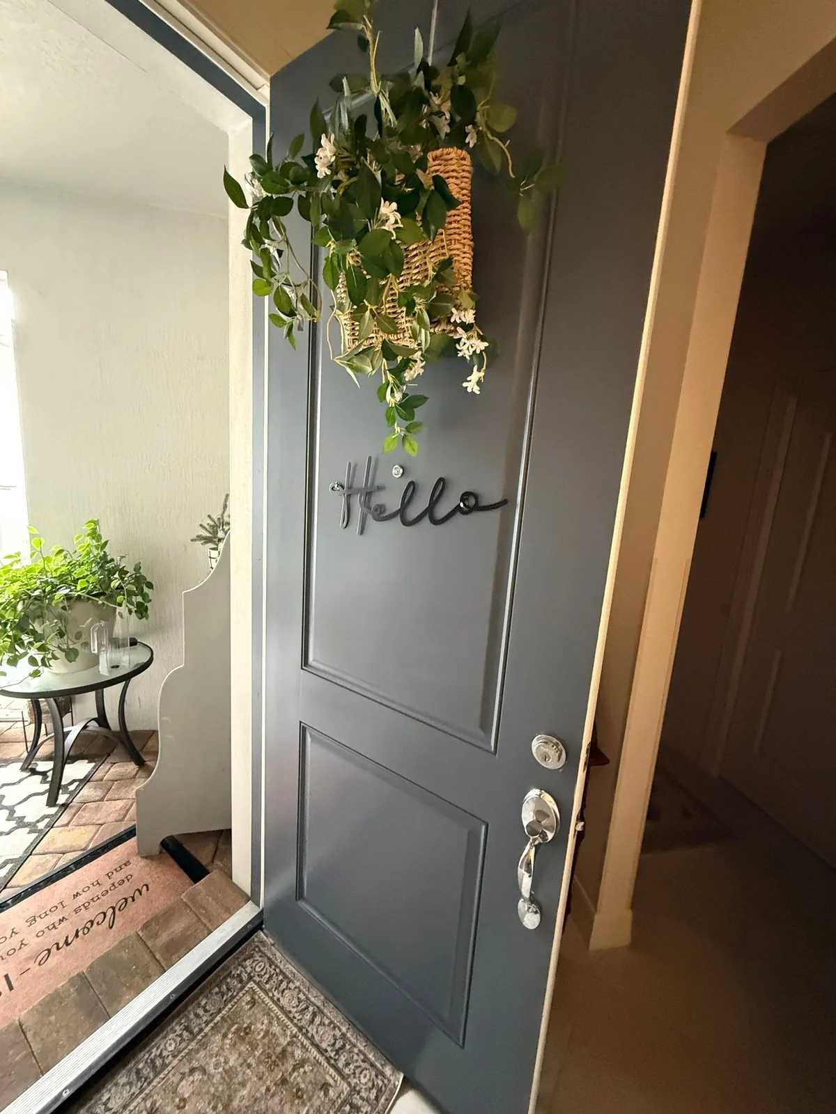 Interior Painting in Port Saint Lucie, Florida. Interior face of a two-panel entry door painted dark slate blue, with a hanging greenery basket and a cursive 'Hello' sign.