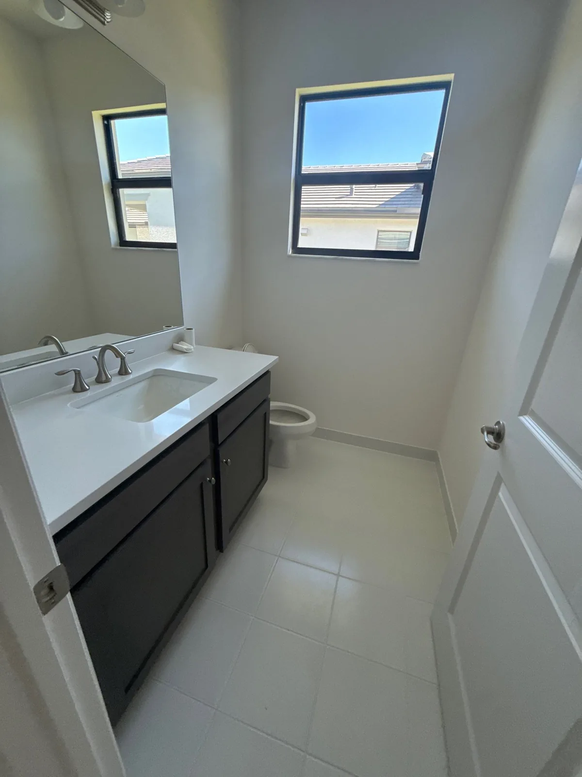 Interior Painting in Port Saint Lucie, Florida. Powder room with white walls, dark vanity cabinet, white countertop and tile floor.