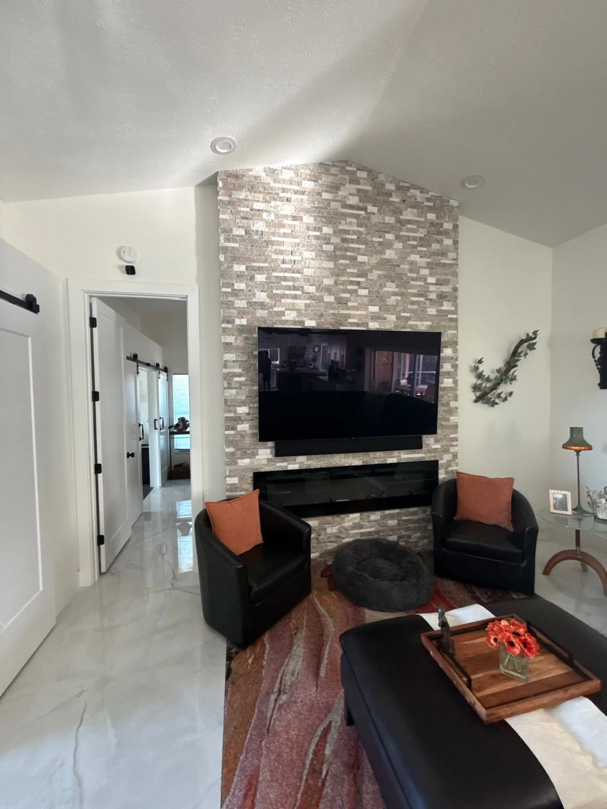 Interior Painting in Port Saint Lucie, Florida. Living room with white painted walls and vaulted ceiling, stacked-stone fireplace wall with wall-mounted television and two dark armchairs.