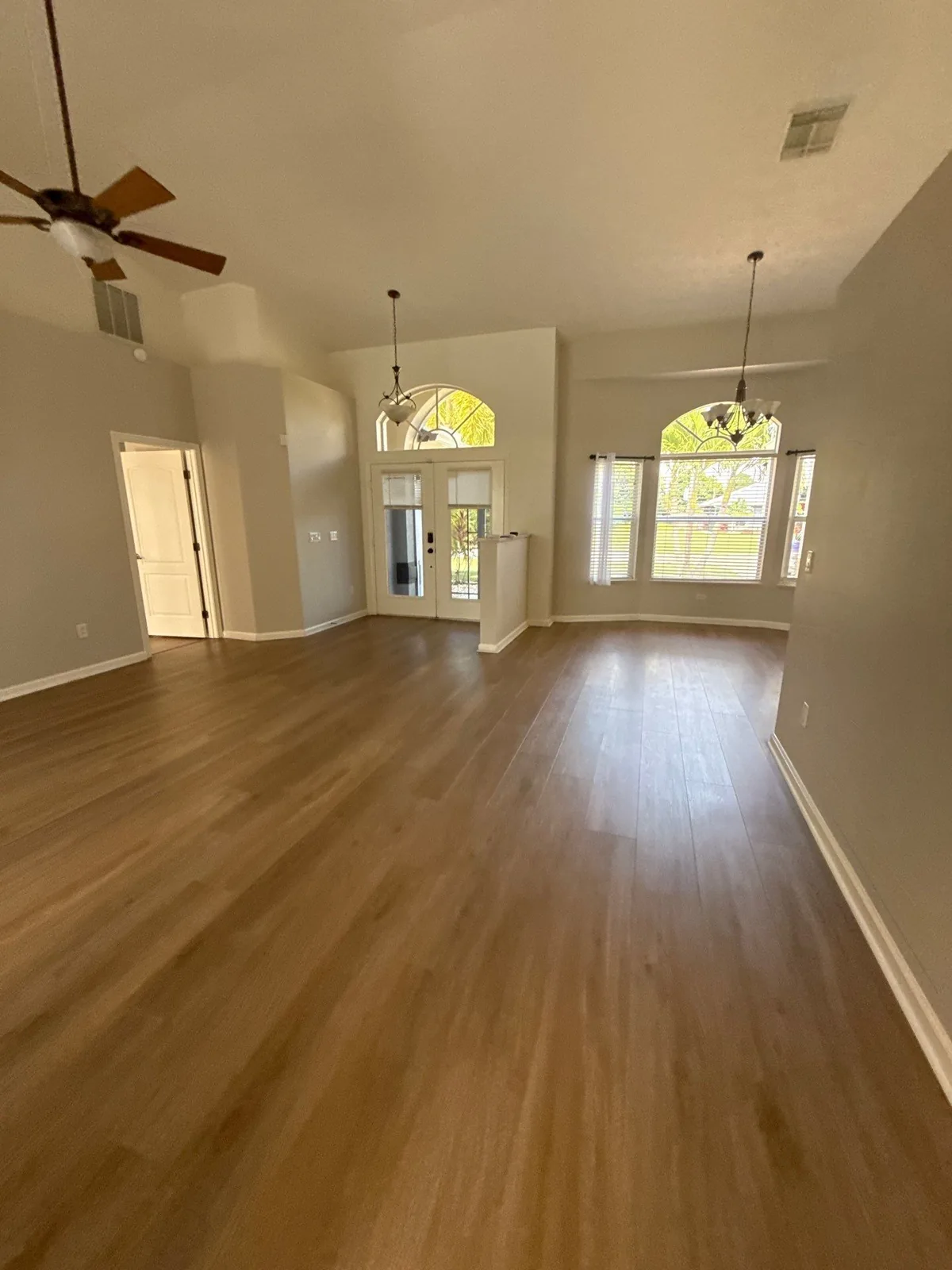 Interior Painting in Port Saint Lucie, Florida. Empty great room with vaulted ceiling, light walls, arched windows and wood-look flooring.