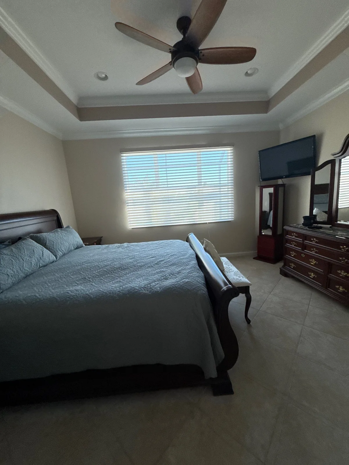 Interior Painting in Port Saint Lucie, Florida. Bedroom with a tray ceiling and crown moulding, neutral painted walls, a made bed and a ceiling fan.