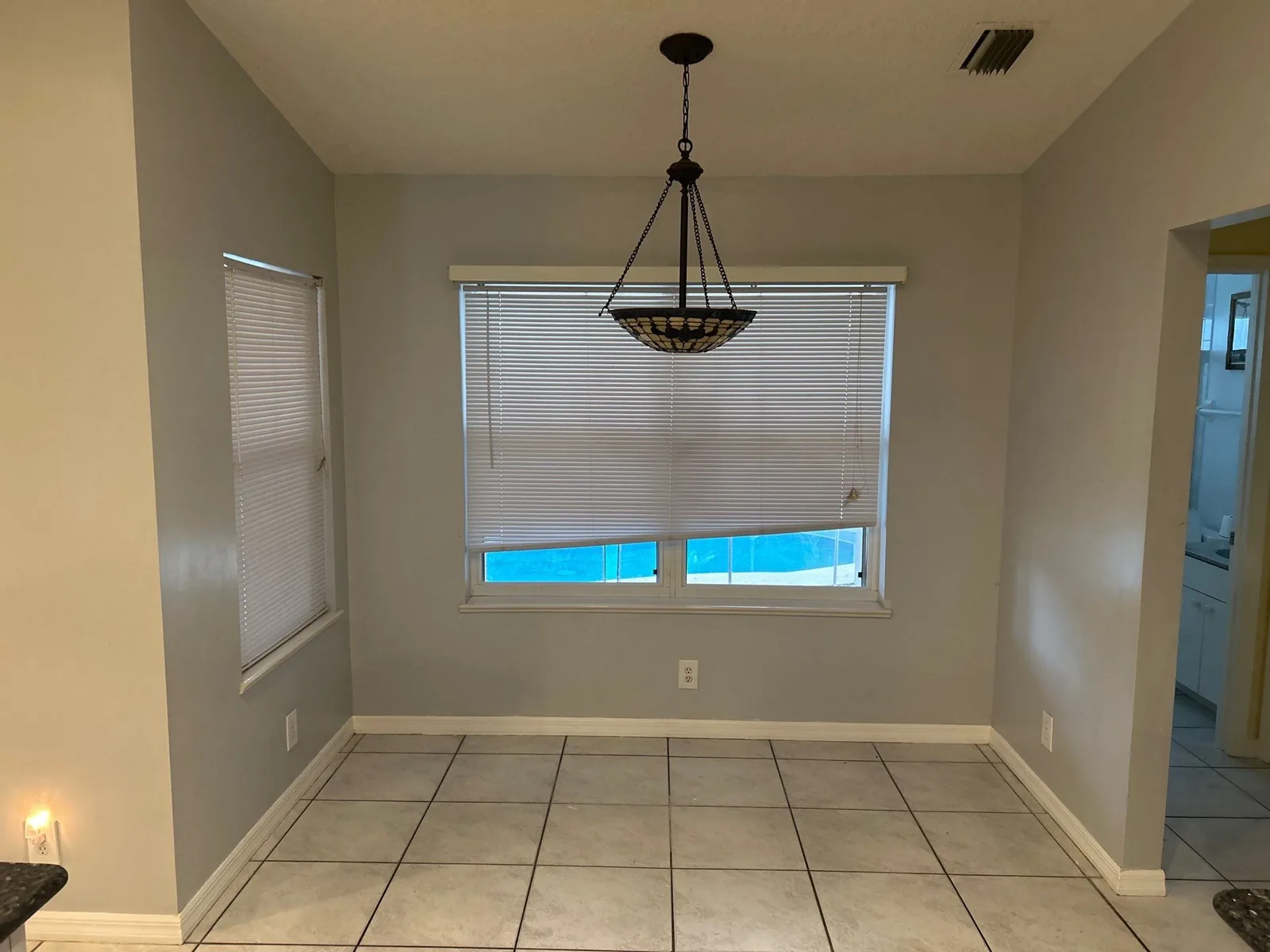 Interior Painting in Port Saint Lucie, Florida. Dining nook with grey painted walls, white window casing and baseboard, pendant light and tile floor.