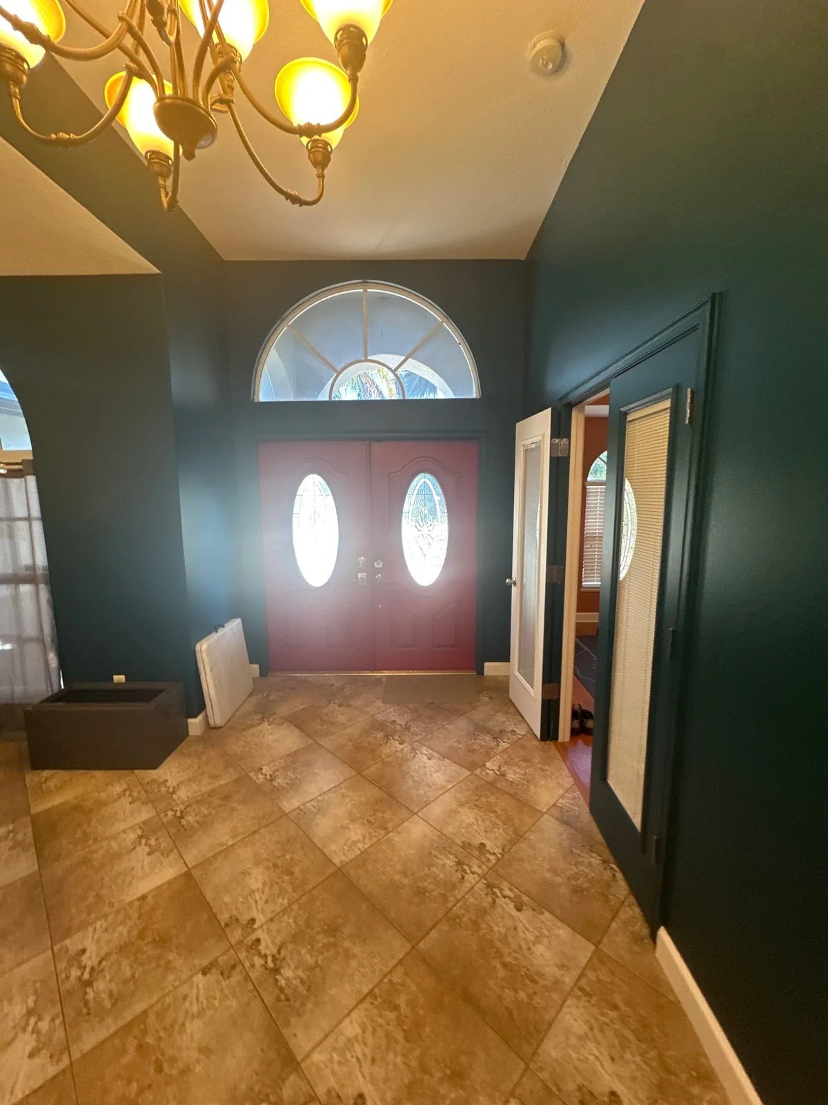 Interior Painting in Port Saint Lucie, Florida. Two-storey entry foyer with dark teal walls, red double front doors with oval glass inserts, arched transom window and tile floor.