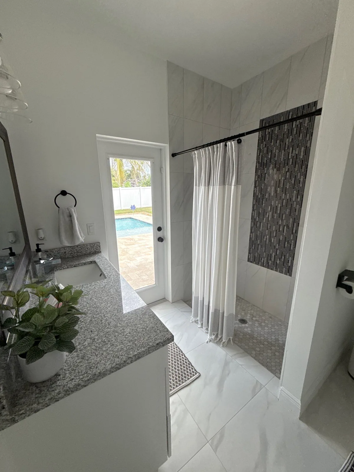 Interior Painting in Port Saint Lucie, Florida. Bathroom with white walls, granite-topped vanity, large-format marble-look tile shower and a glazed door to a pool deck.