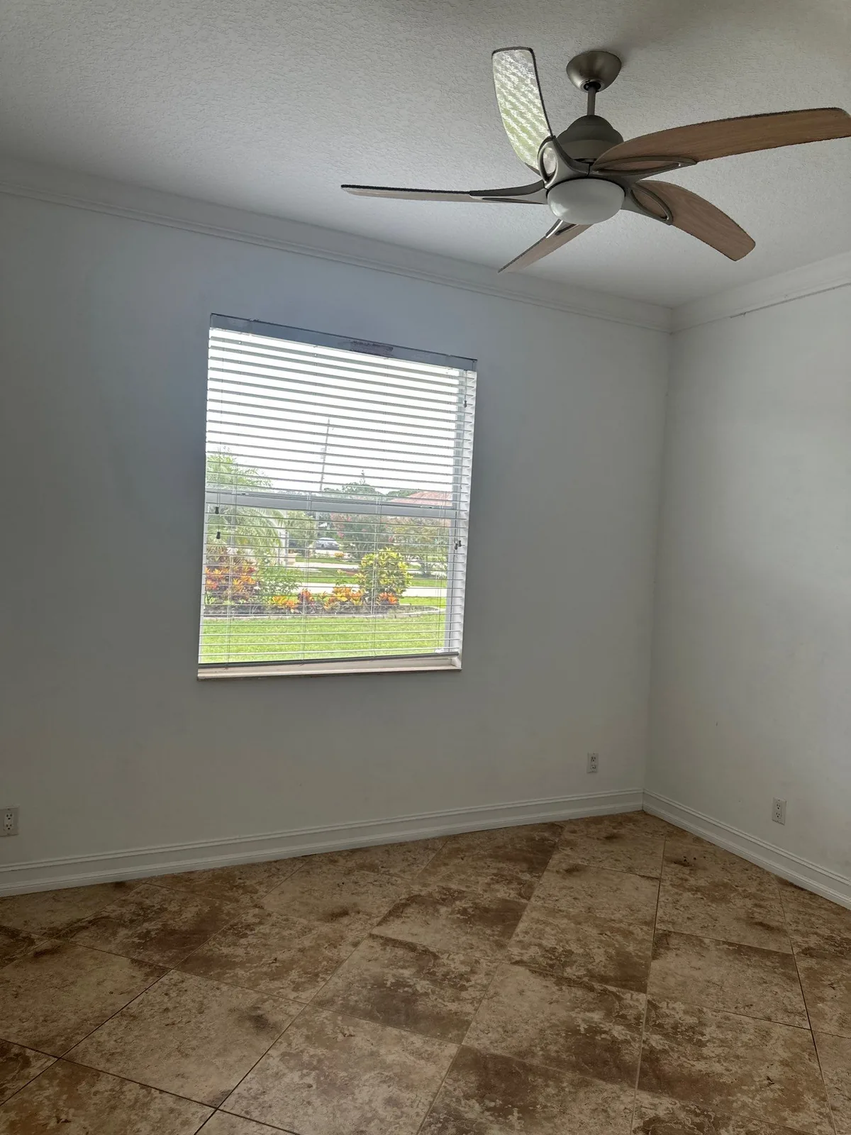 Interior Painting in Port Saint Lucie, Florida. Empty room with white painted walls, textured ceiling, ceiling fan and a single window with blinds looking onto grass.