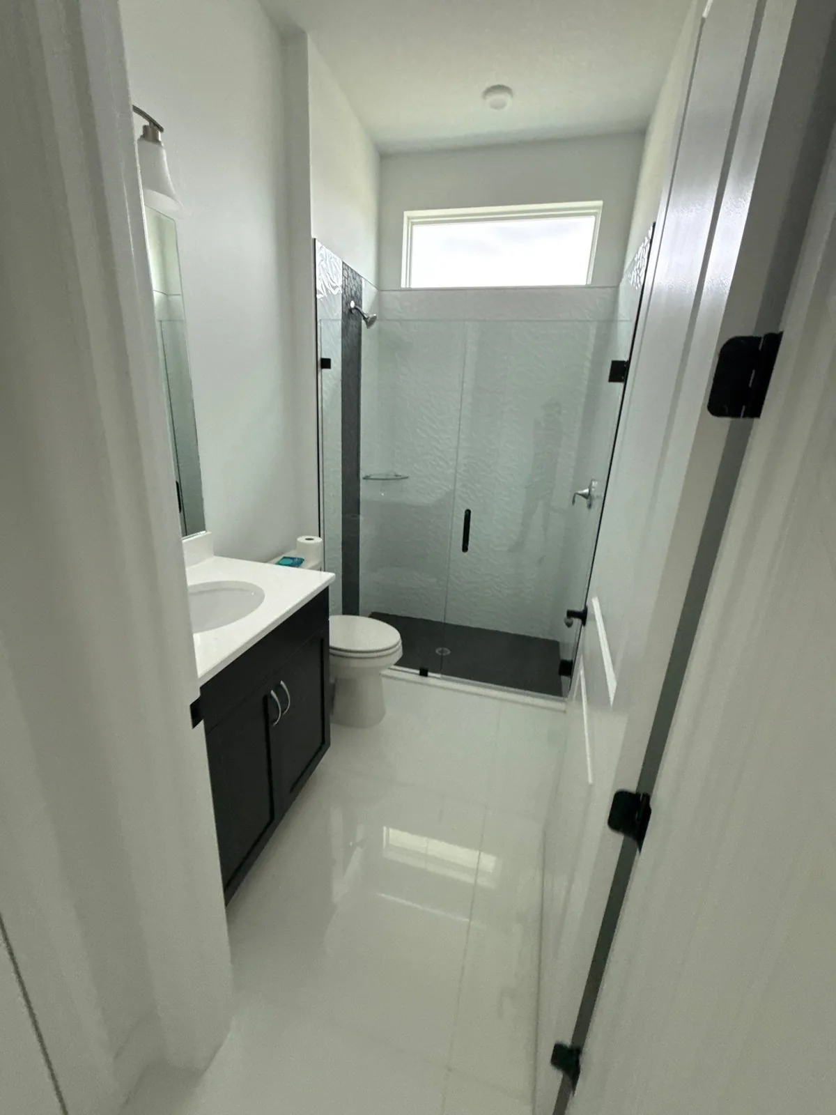 Interior Painting in Port Saint Lucie, Florida. Bathroom with white walls, glass shower enclosure, dark vanity and white tile floor.