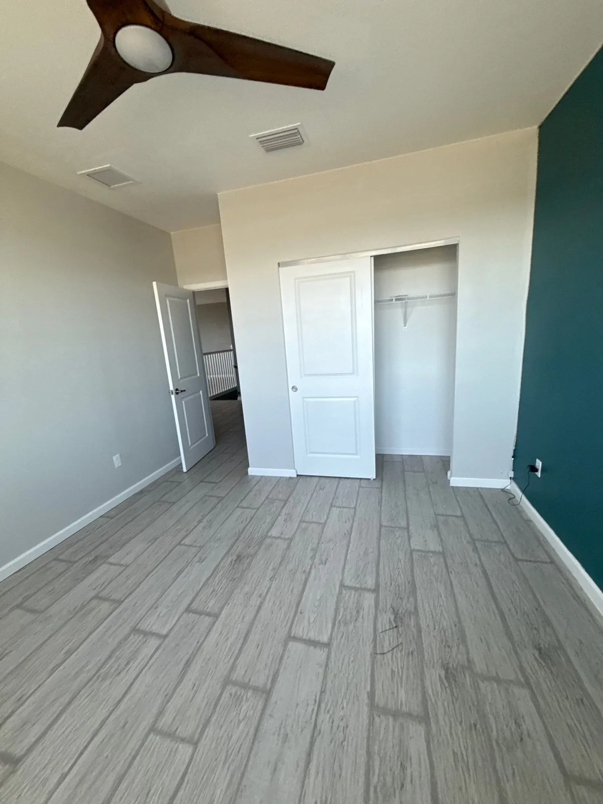 Interior Painting in Port Saint Lucie, Florida. Empty bedroom with white walls, a teal accent wall, open closet with white door and wood-look plank flooring.