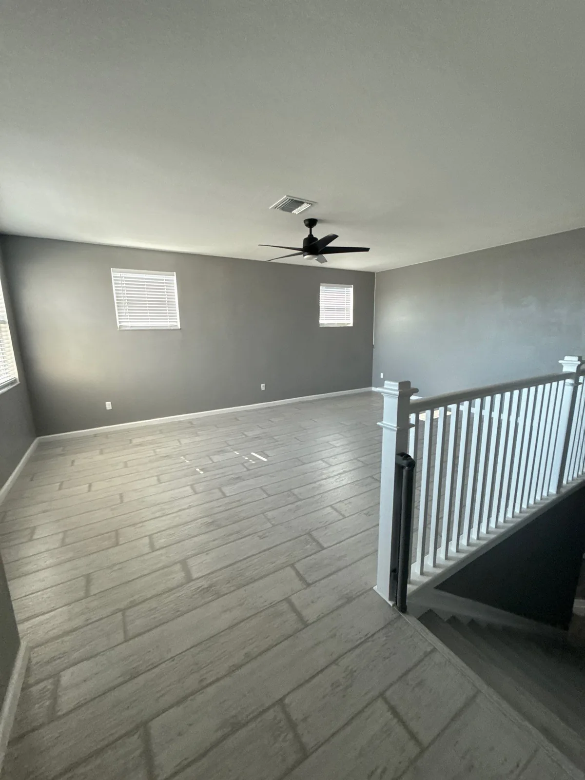 Interior Painting in Port Saint Lucie, Florida. Empty room with grey painted walls, white baseboards and a white stair railing, wood-look tile flooring.