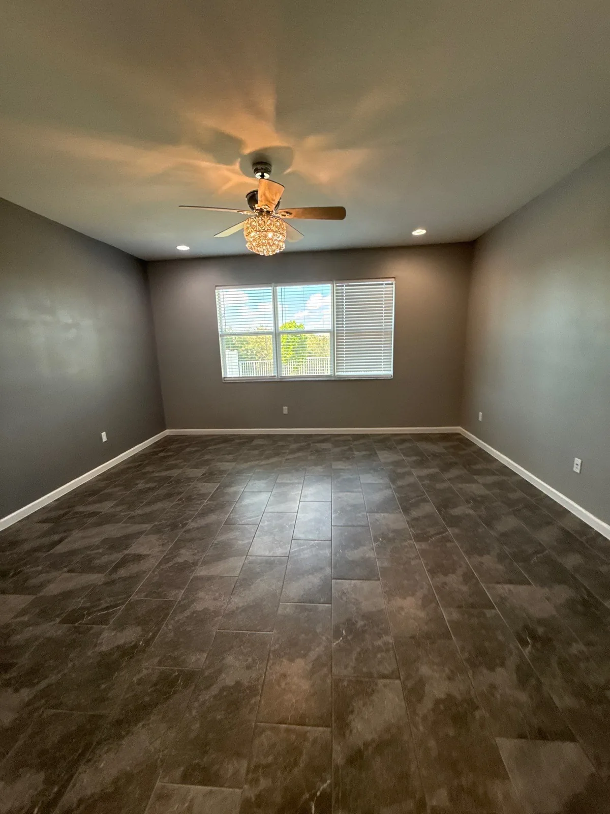 Interior Painting in Port Saint Lucie, Florida. Empty bedroom with grey walls and white trim, ceiling fan with light on and a window with blinds.