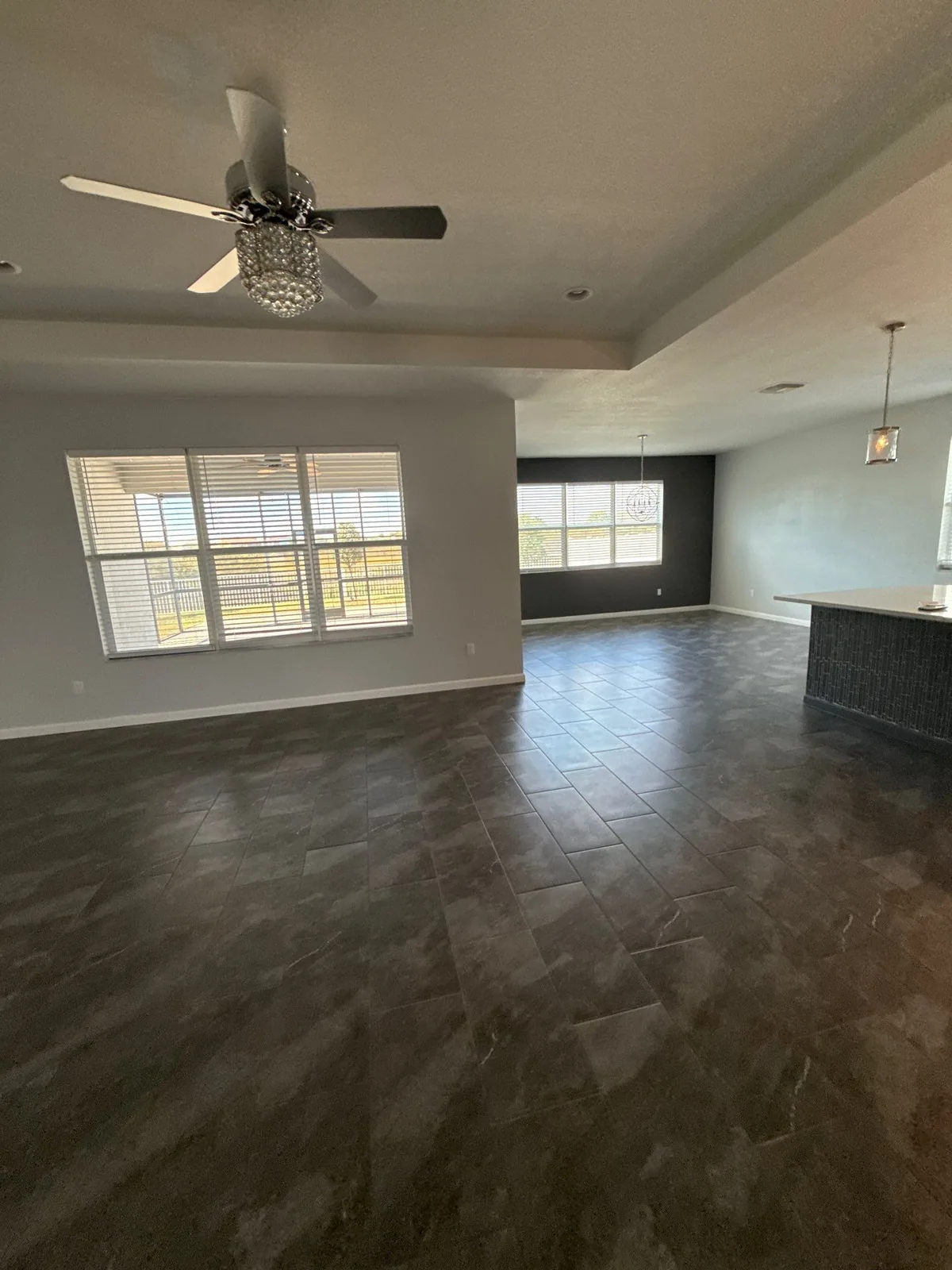 Interior Painting in Port Saint Lucie, Florida. Empty open-plan living and dining area with light grey walls, a tray ceiling, a dark accent wall and dark tile floor.