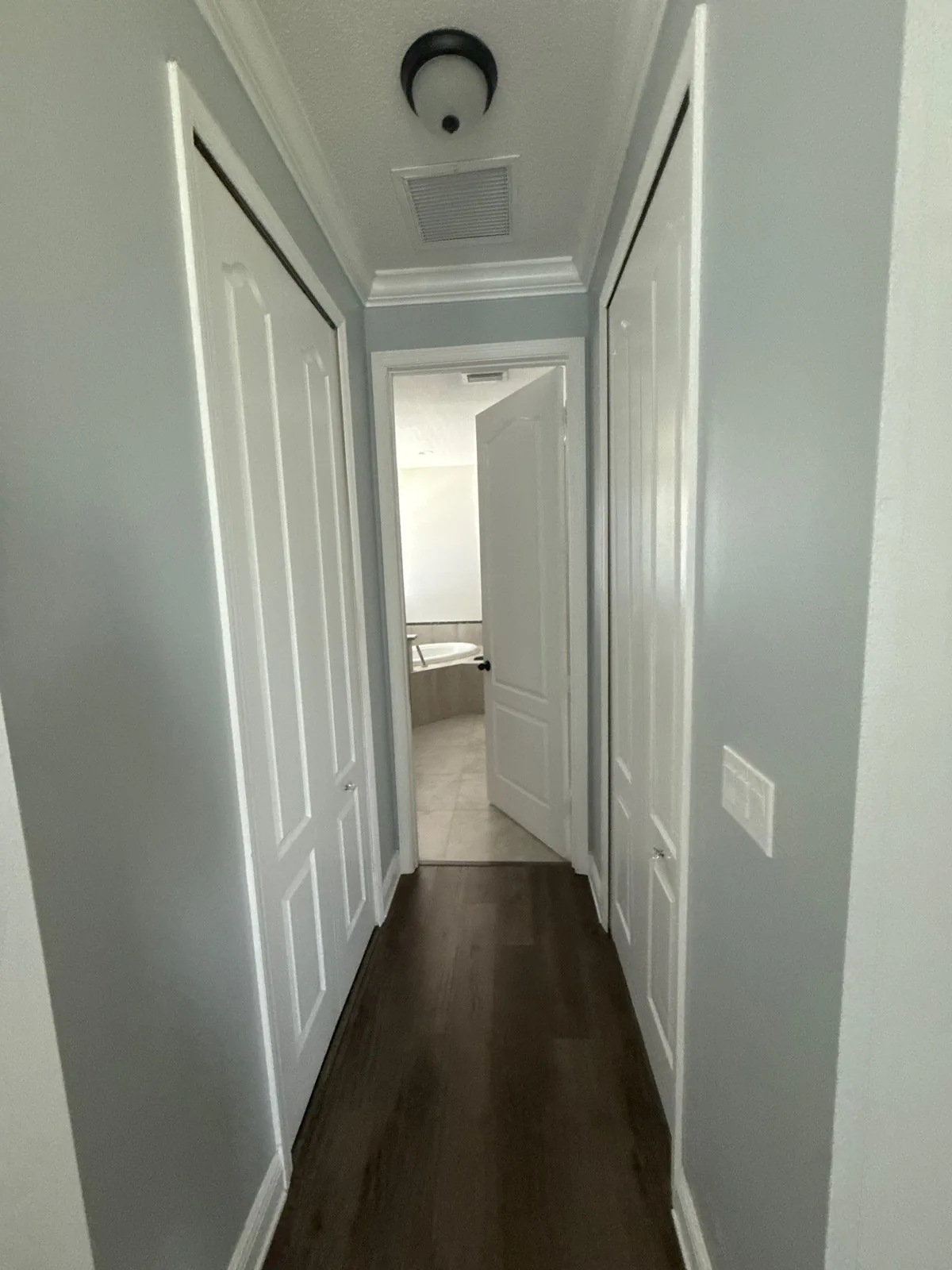 Interior Painting in Port Saint Lucie, Florida. Hallway with light grey walls, white doors, white crown moulding and baseboards, dark wood-look flooring.