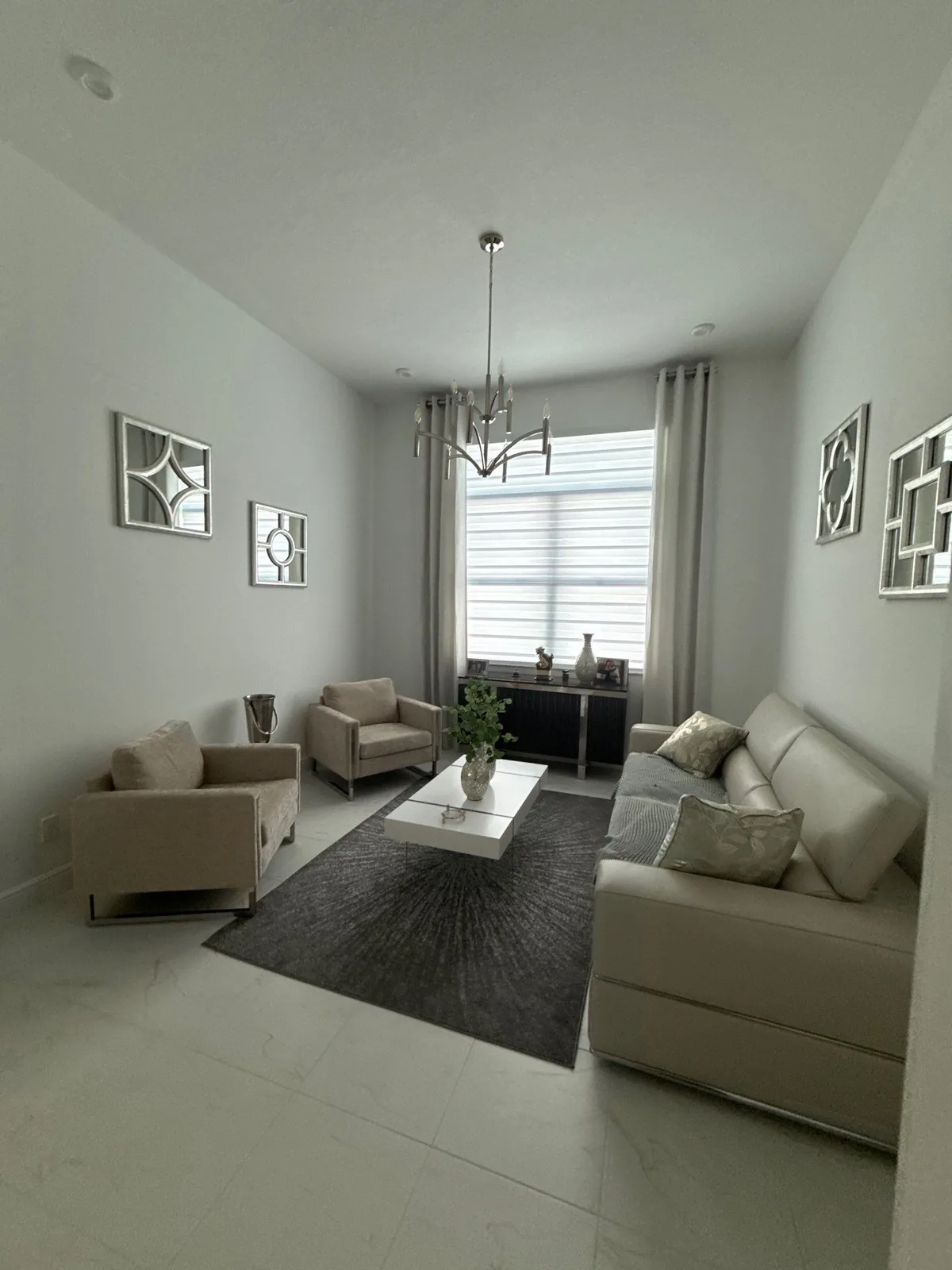 Interior Painting in Port Saint Lucie, Florida. Living room with pale painted walls and white ceiling, chandelier, curtained window and staged seating.
