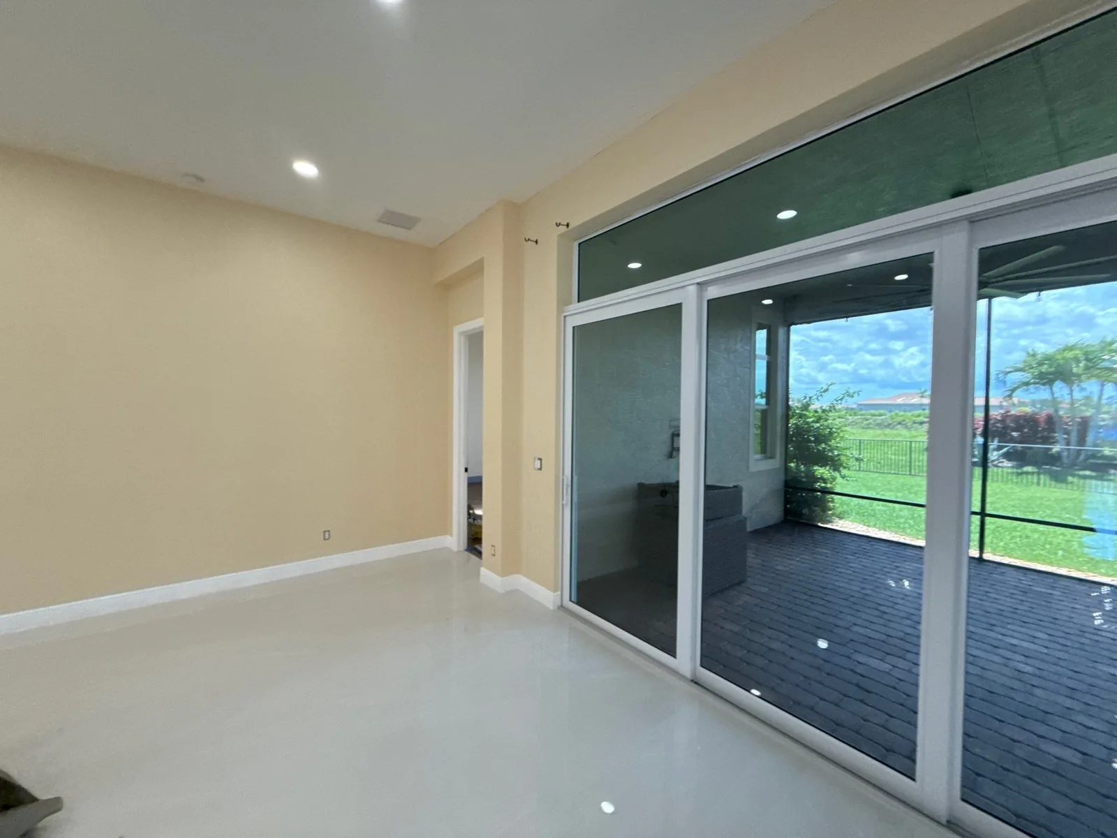 Interior Painting in Port Saint Lucie, Florida. Empty room with tan walls, white ceiling and baseboards, recessed lights and a wall of sliding glass doors onto a covered patio.