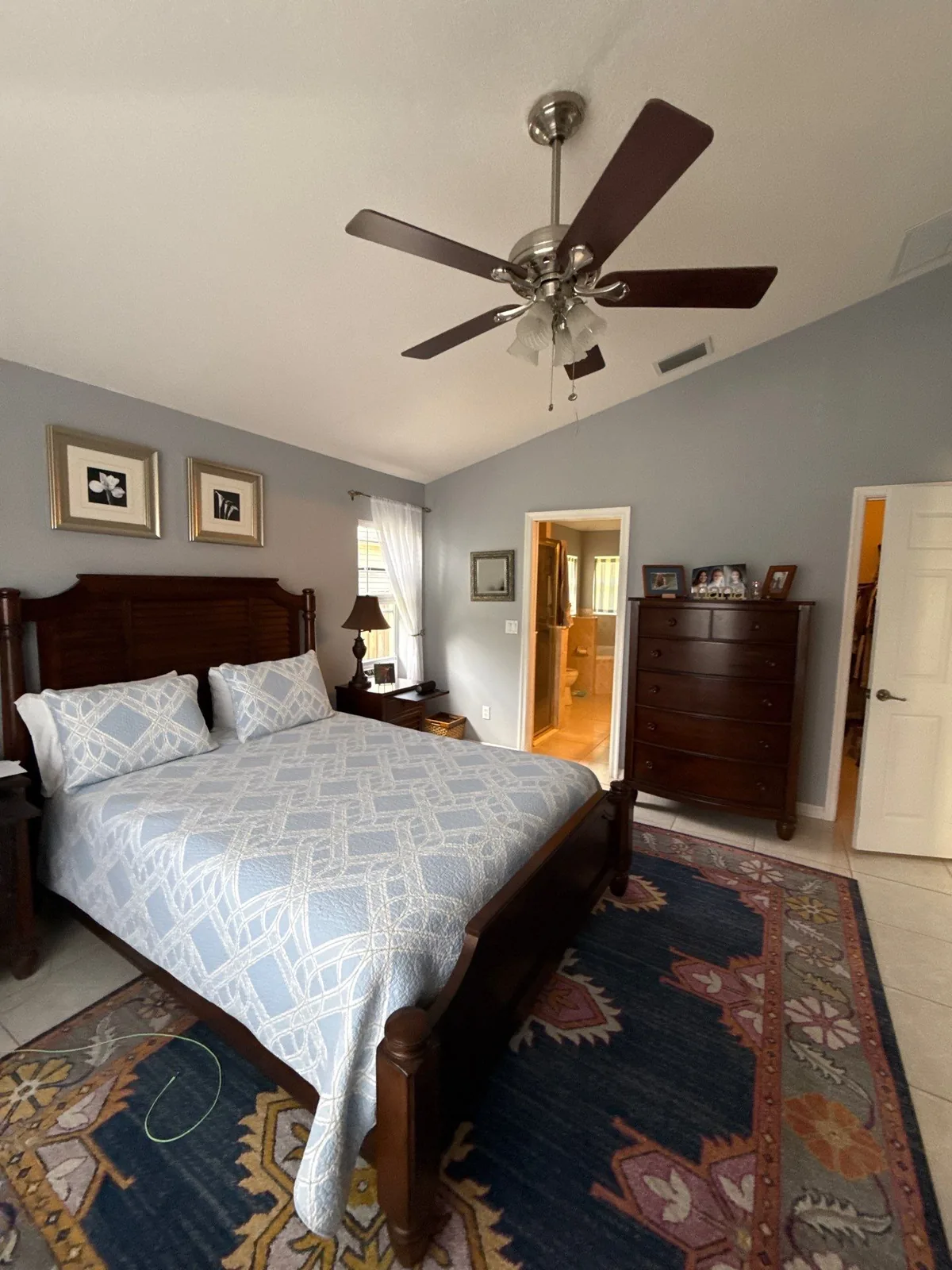 Interior Painting in Port Saint Lucie, Florida. Bedroom with grey-blue walls and white ceiling, ceiling fan, dark wood bed and dresser over a patterned rug.