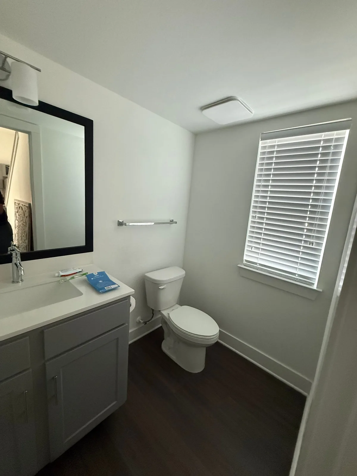 Interior Painting in Port Saint Lucie, Florida. Finished bathroom with light grey walls, white ceiling and trim, grey vanity with white countertop, toilet and a window with white blinds.