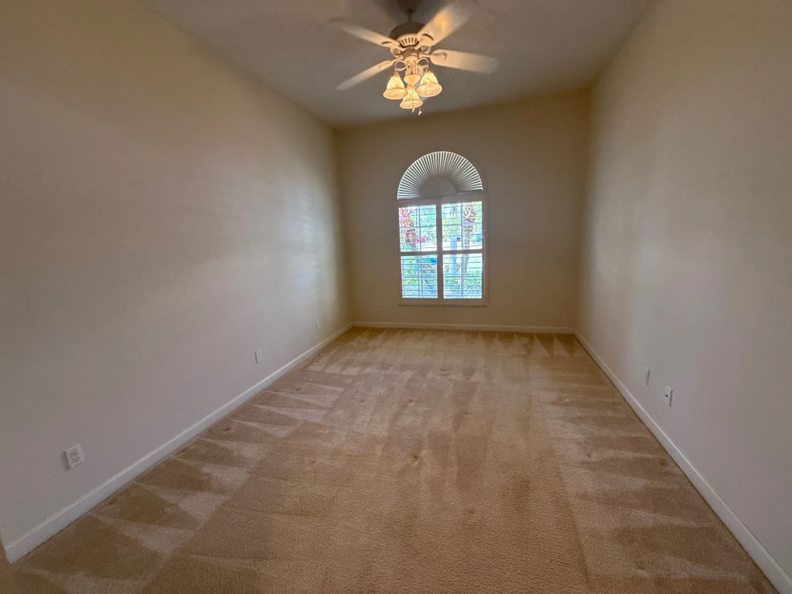 Interior Painting in Port Saint Lucie, Florida. Empty bedroom with freshly painted light walls, white baseboards, an arched window and carpet.